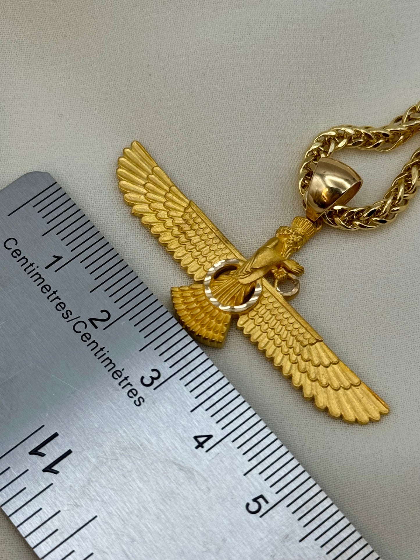 Gold eagle pendant with chain next to a ruler for scale on a light gray background