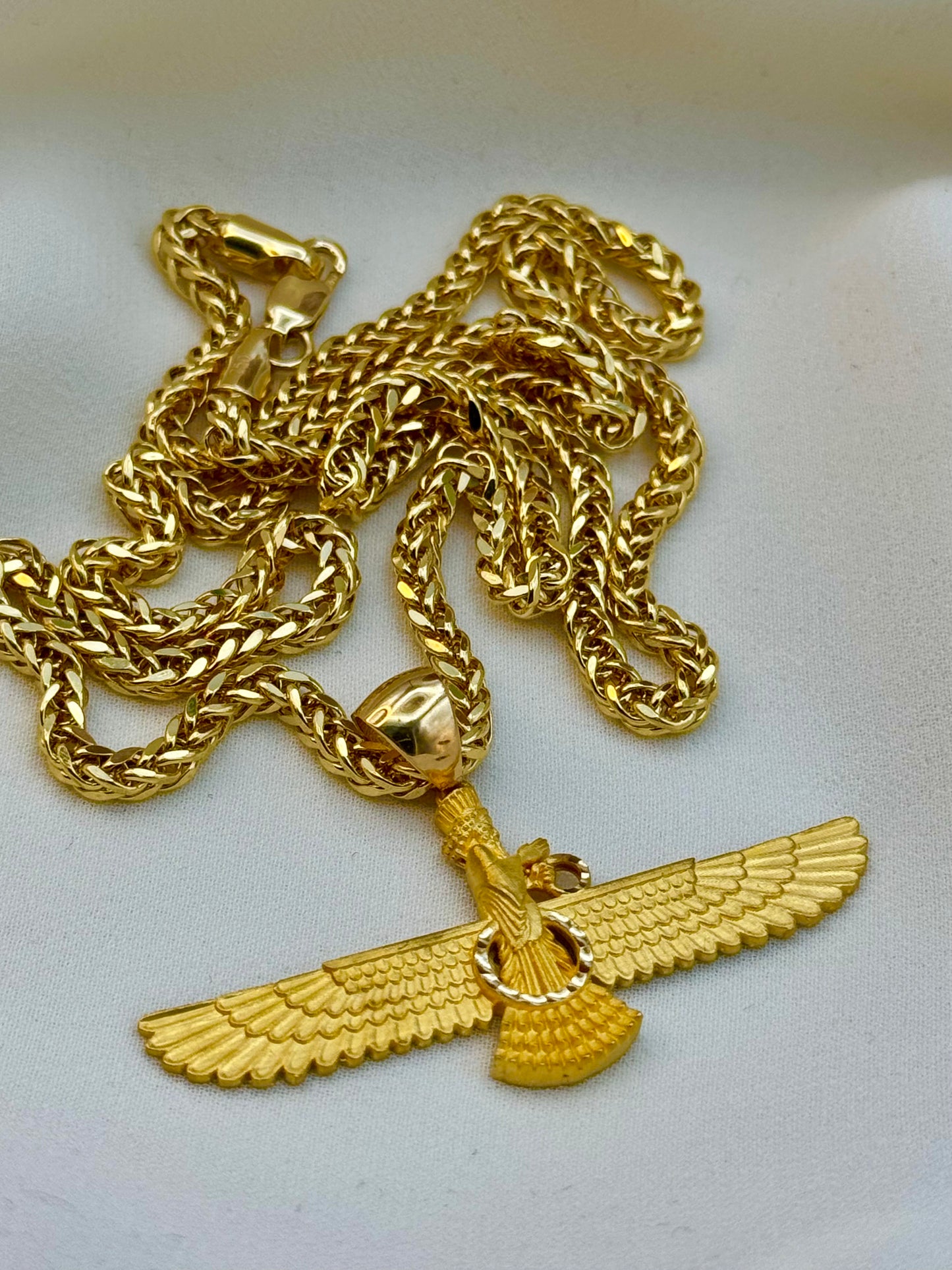 Gold chain with an eagle pendant on a light gray background