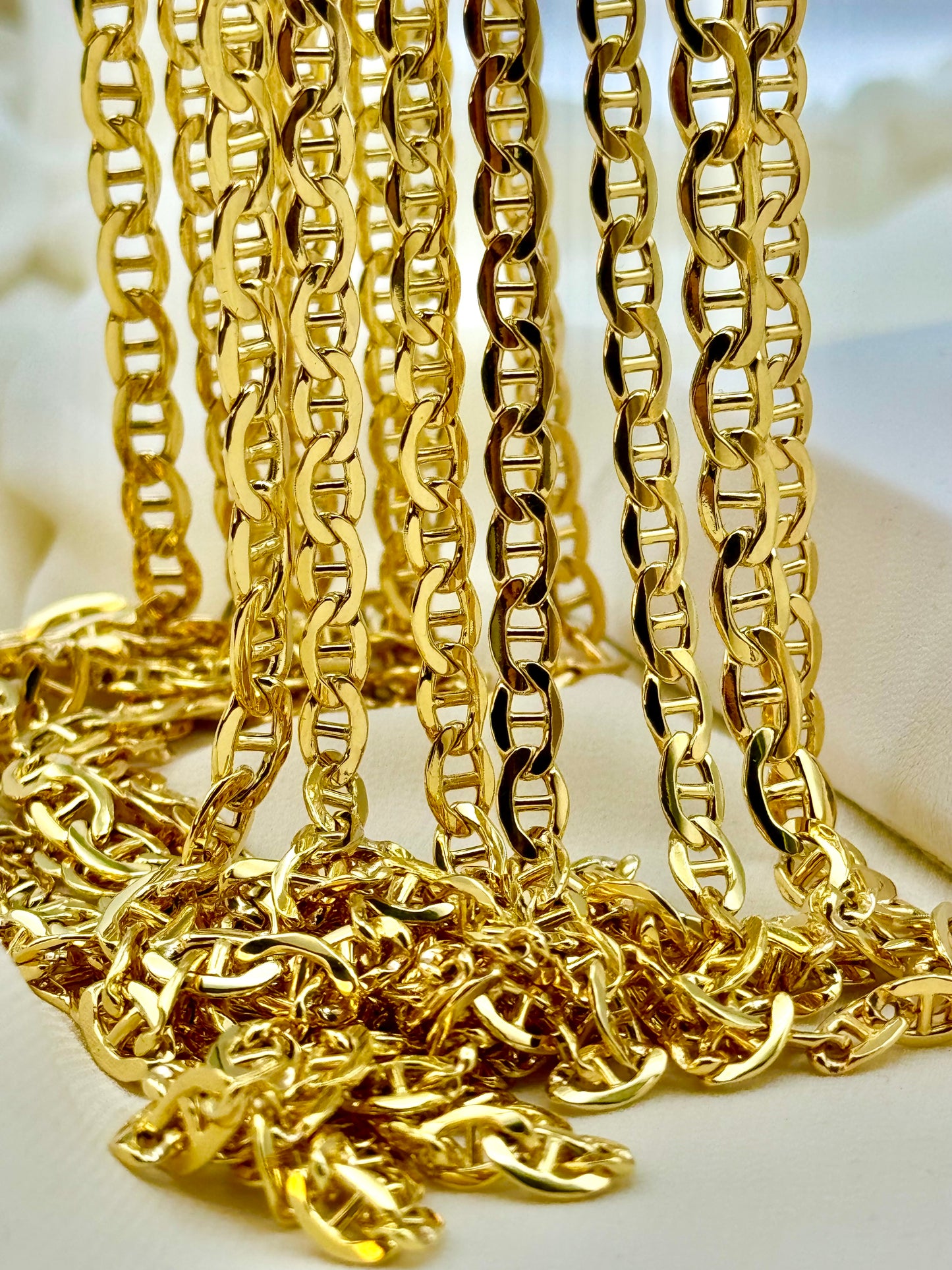 A 14K gold anchor chain necklace with a lobster hook clasp, laid out in a semi-circular shape on a light surface.