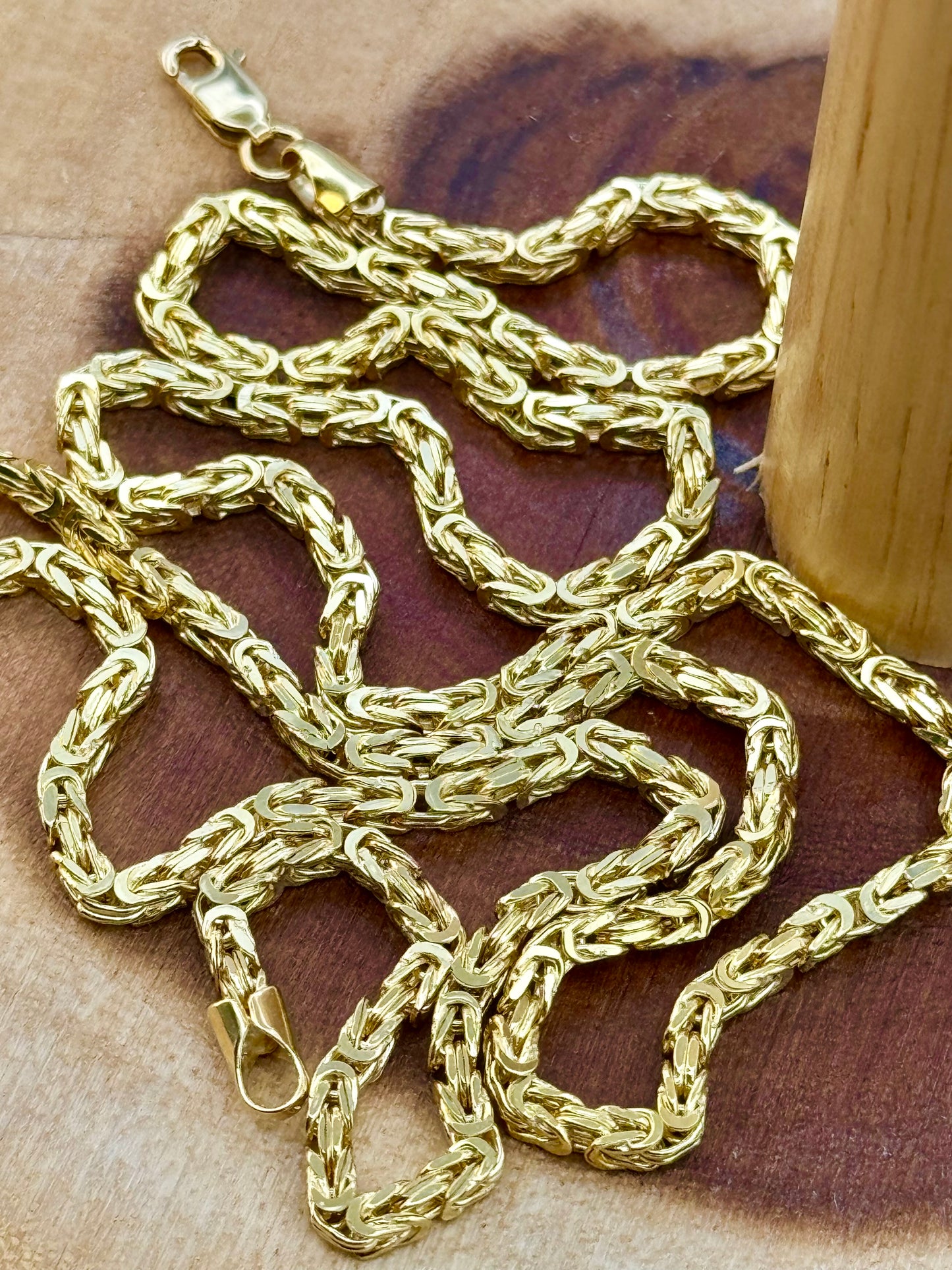 An 18K solid gold byzantine chain necklace laid out on a wooden surface, showcasing its 3mm thickness and 23.5 inches length.