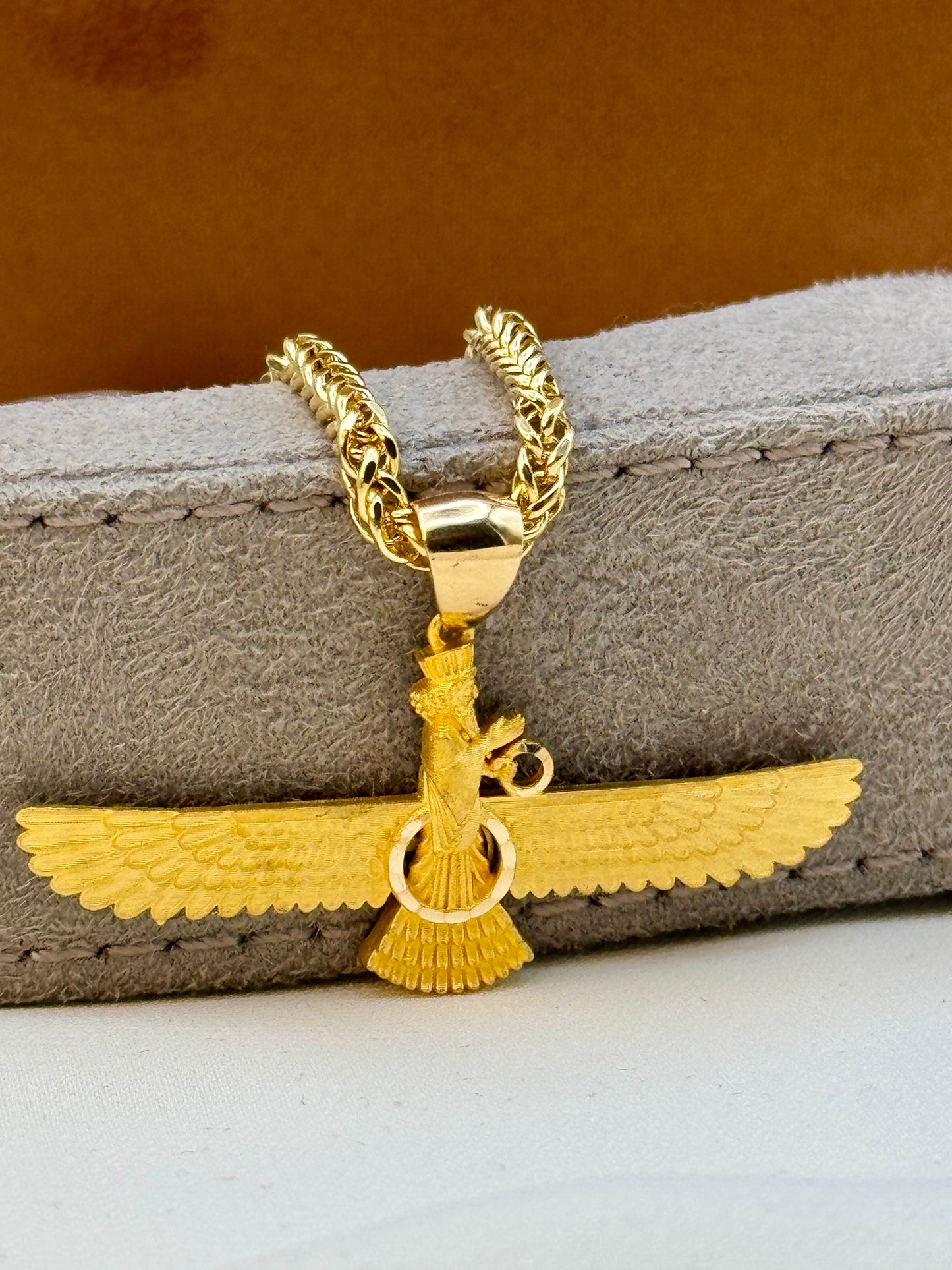 Faravahar Gold necklace with a unique pendant on a textured surface