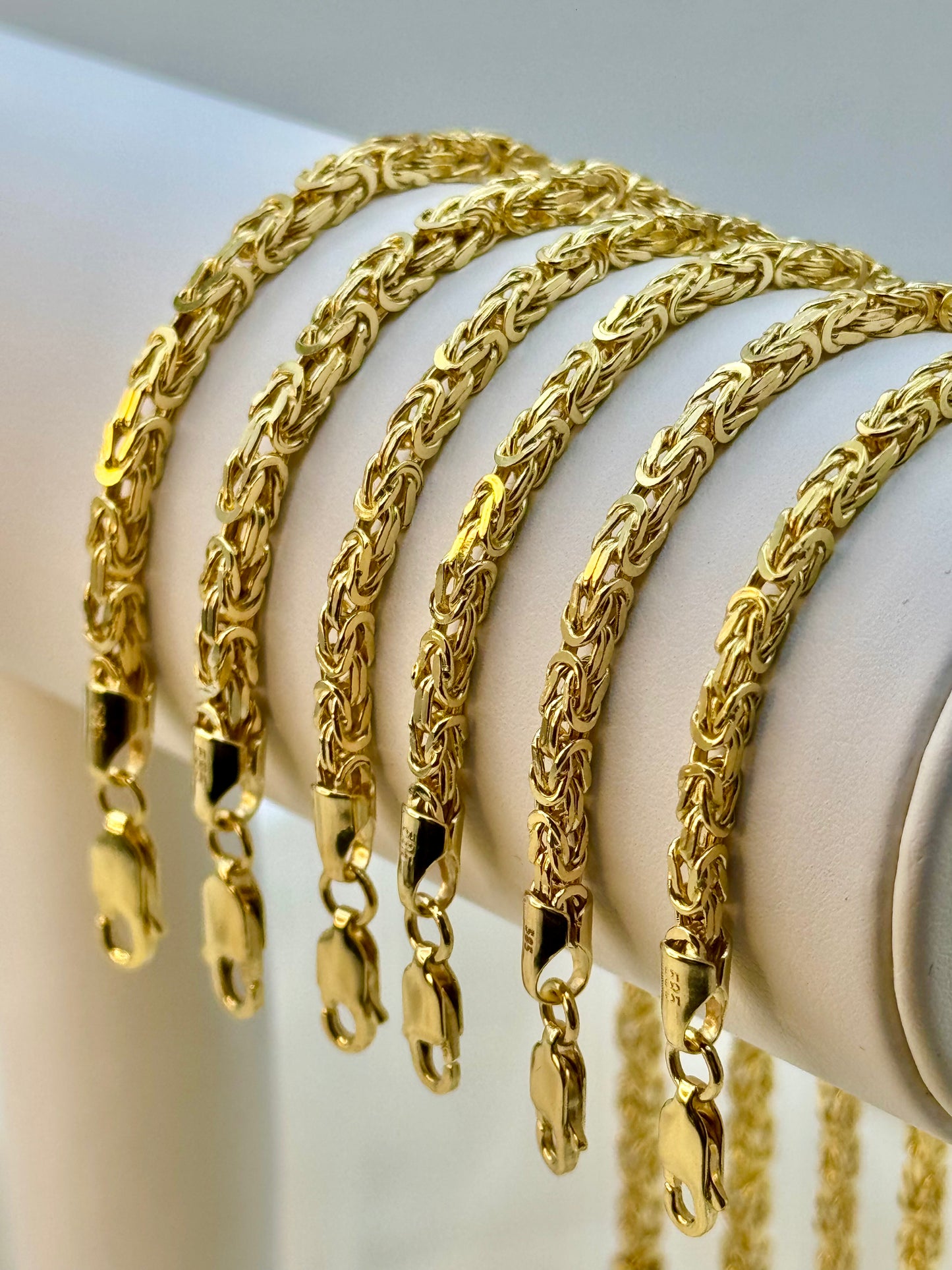 A collection of 14K gold Byzantine bracelets displayed on a stand, showcasing the chain link design and gold thickness.