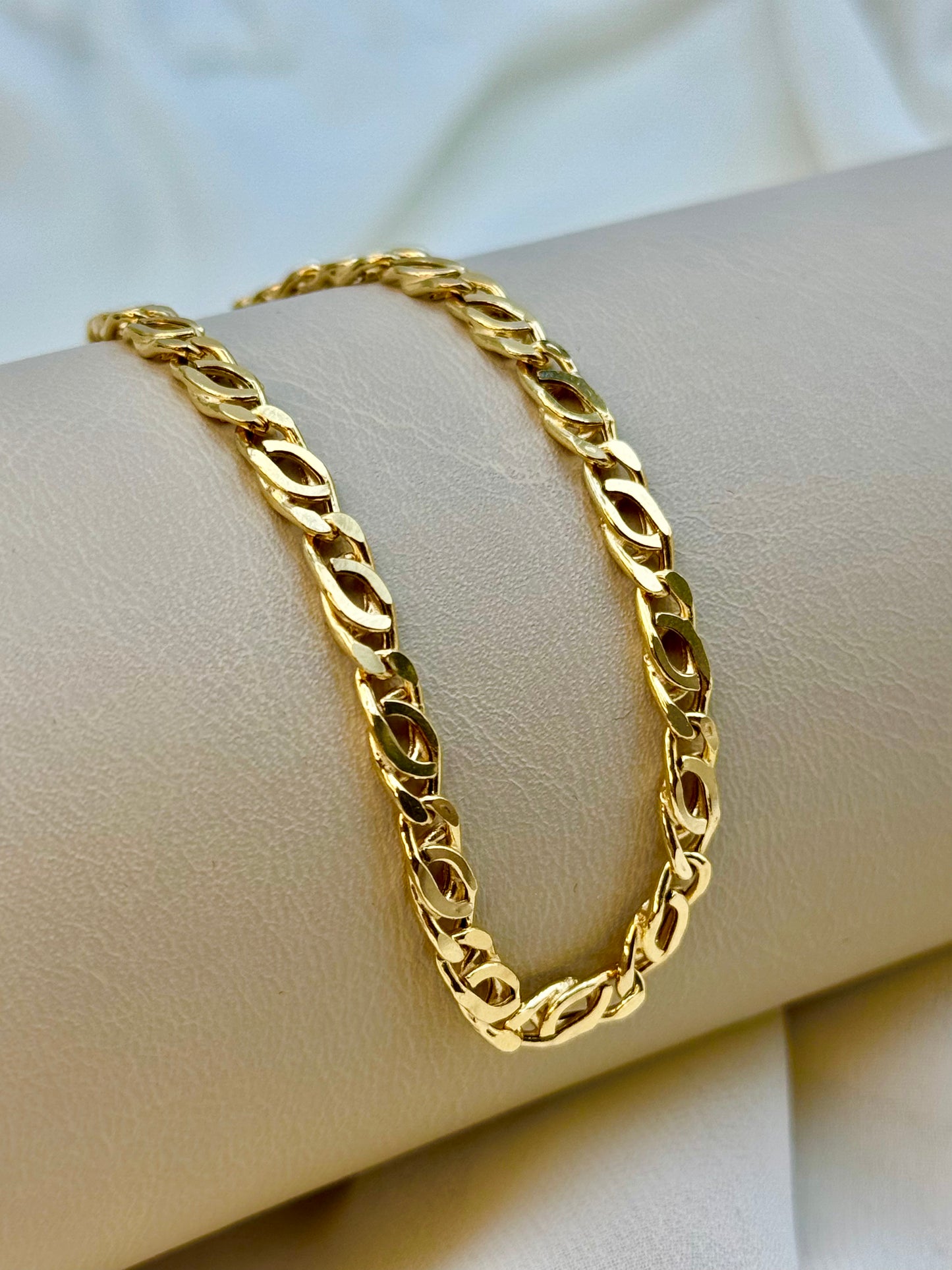 A gold curb bracelet displayed on a cylindrical stand, with a classic double curb link design.