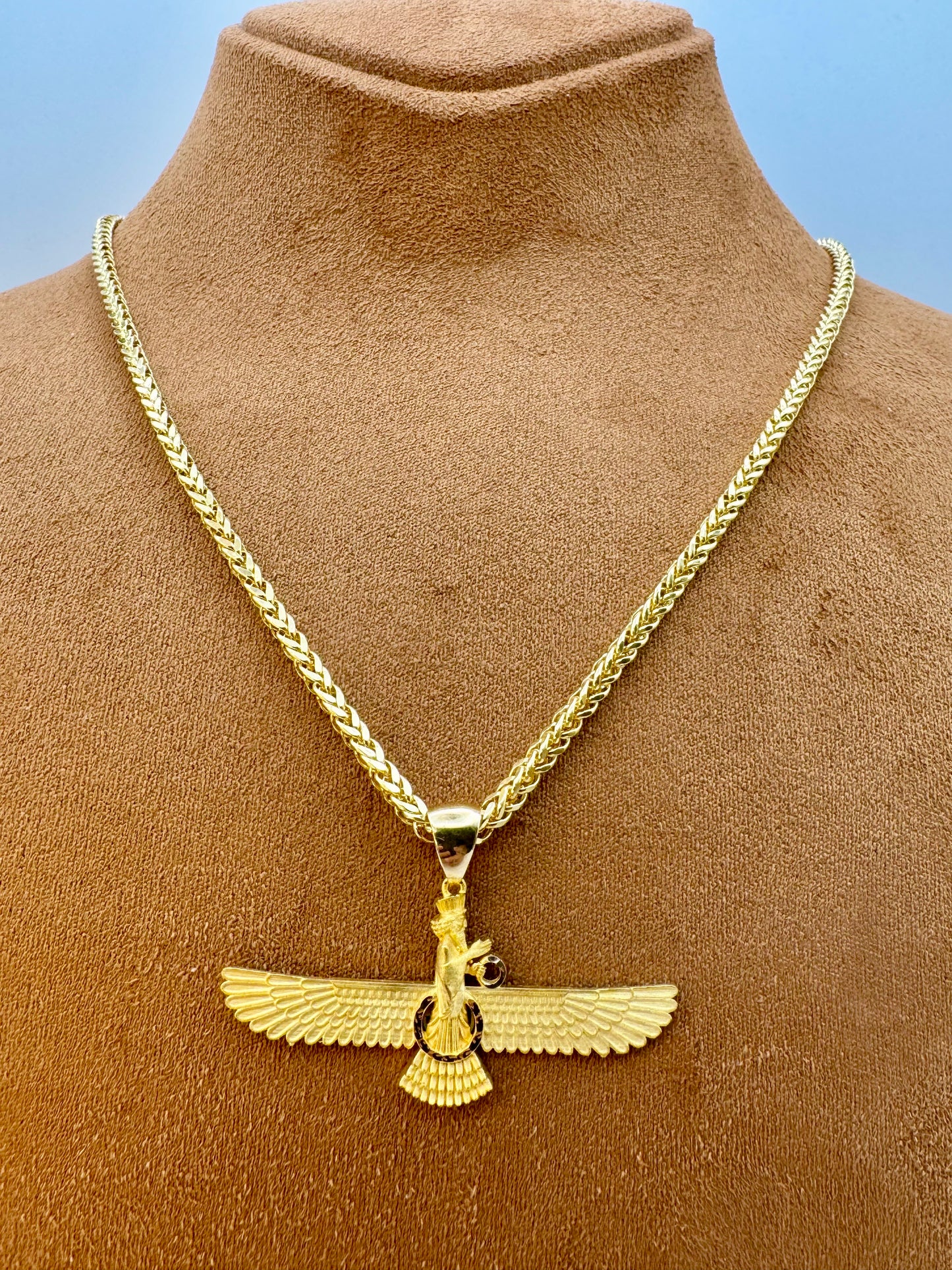 Gold necklace with a winged pendant on a brown mannequin