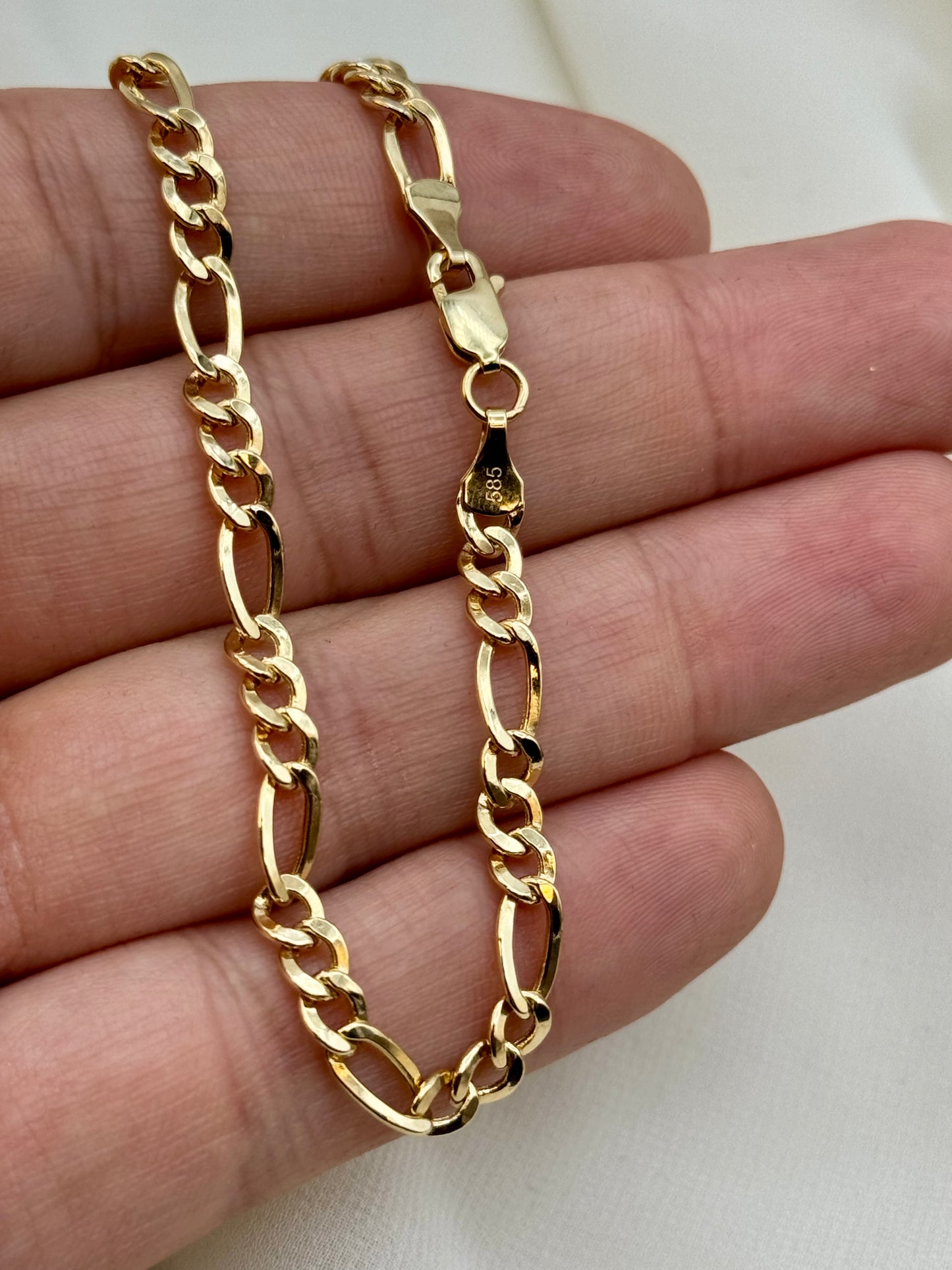 Gold chain necklace held on a hand against a white background