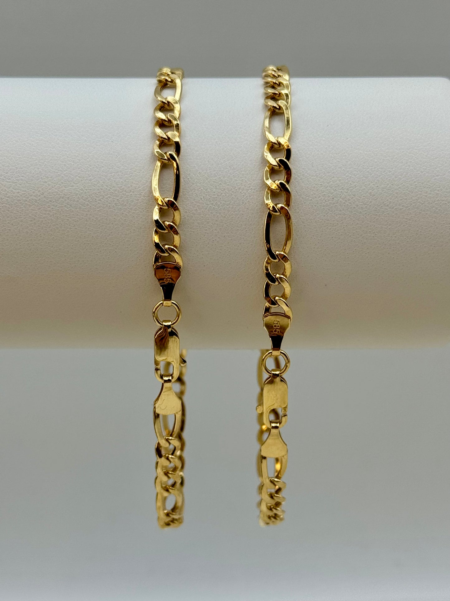 Two gold figaro chain bracelets on a white surface