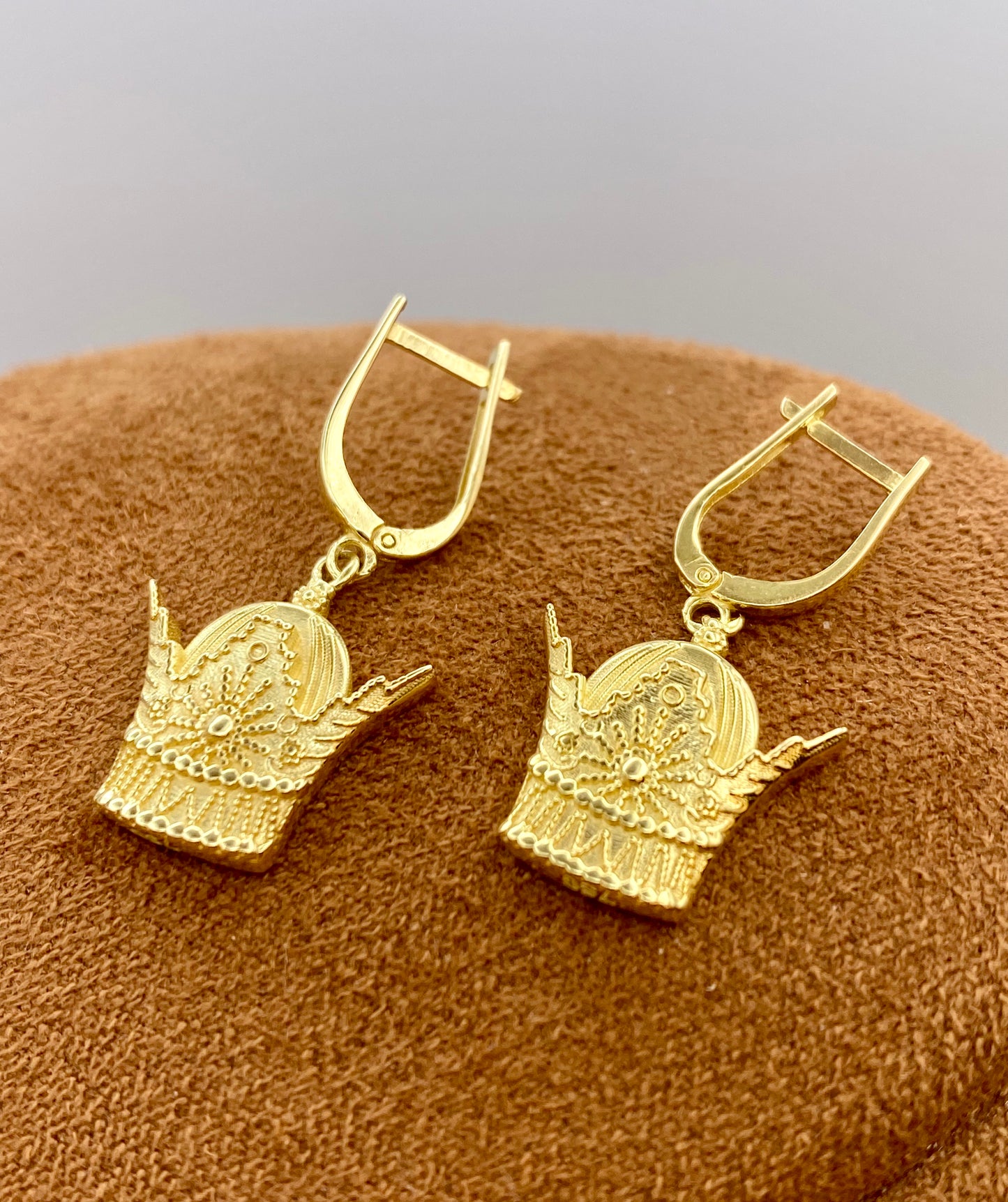 Gold earrings on a brown textured surface with a gray background