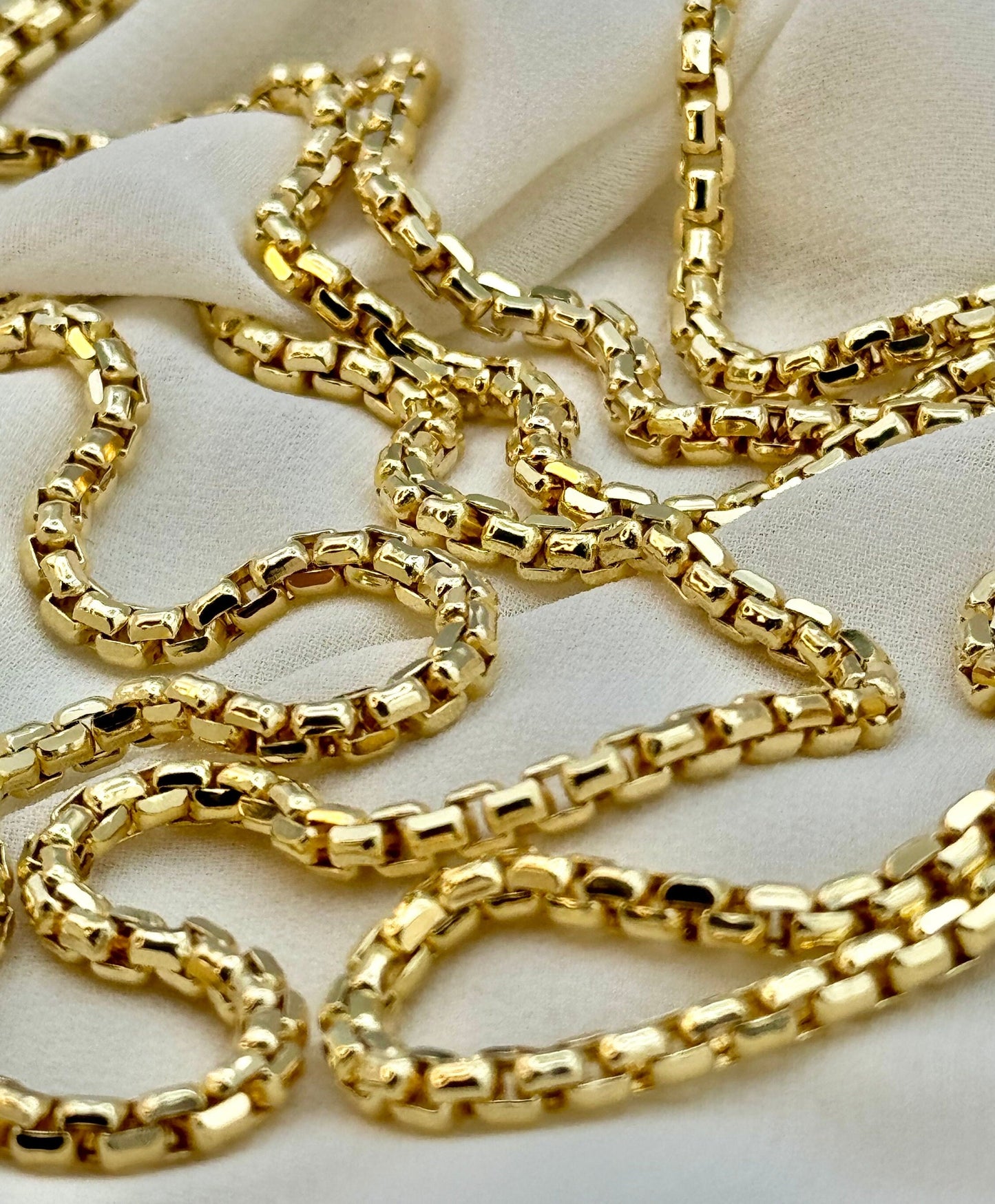 A 14k gold box chain necklace laid out on a white surface.