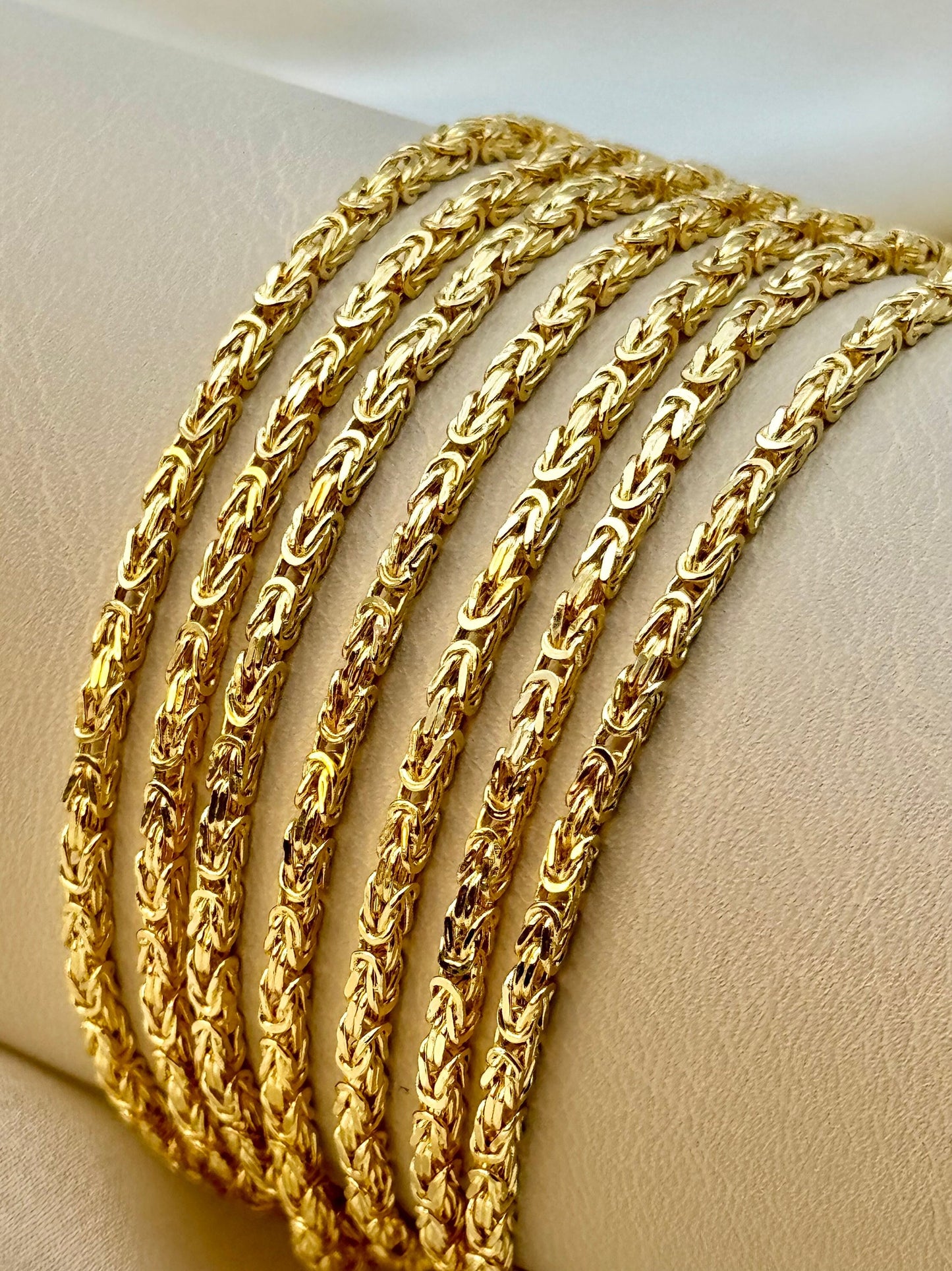 A collection of 18K gold Byzantine chain necklaces displayed on a mannequin, showing the texture and link design of the chains.