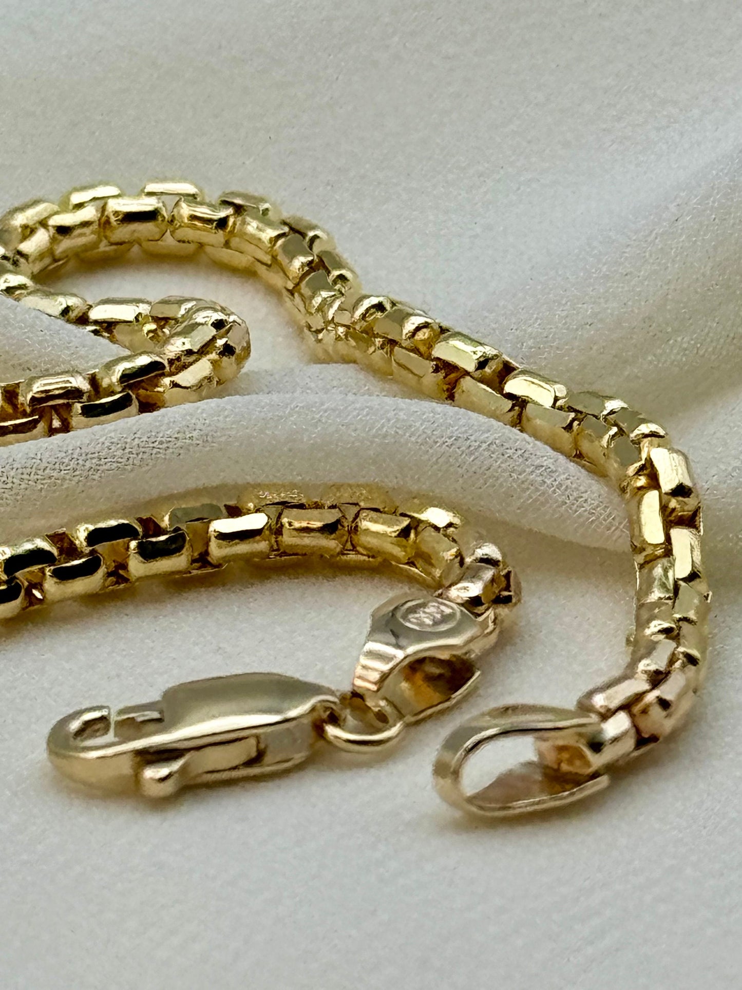 A 14K gold box chain bracelet displayed on a white fabric surface.