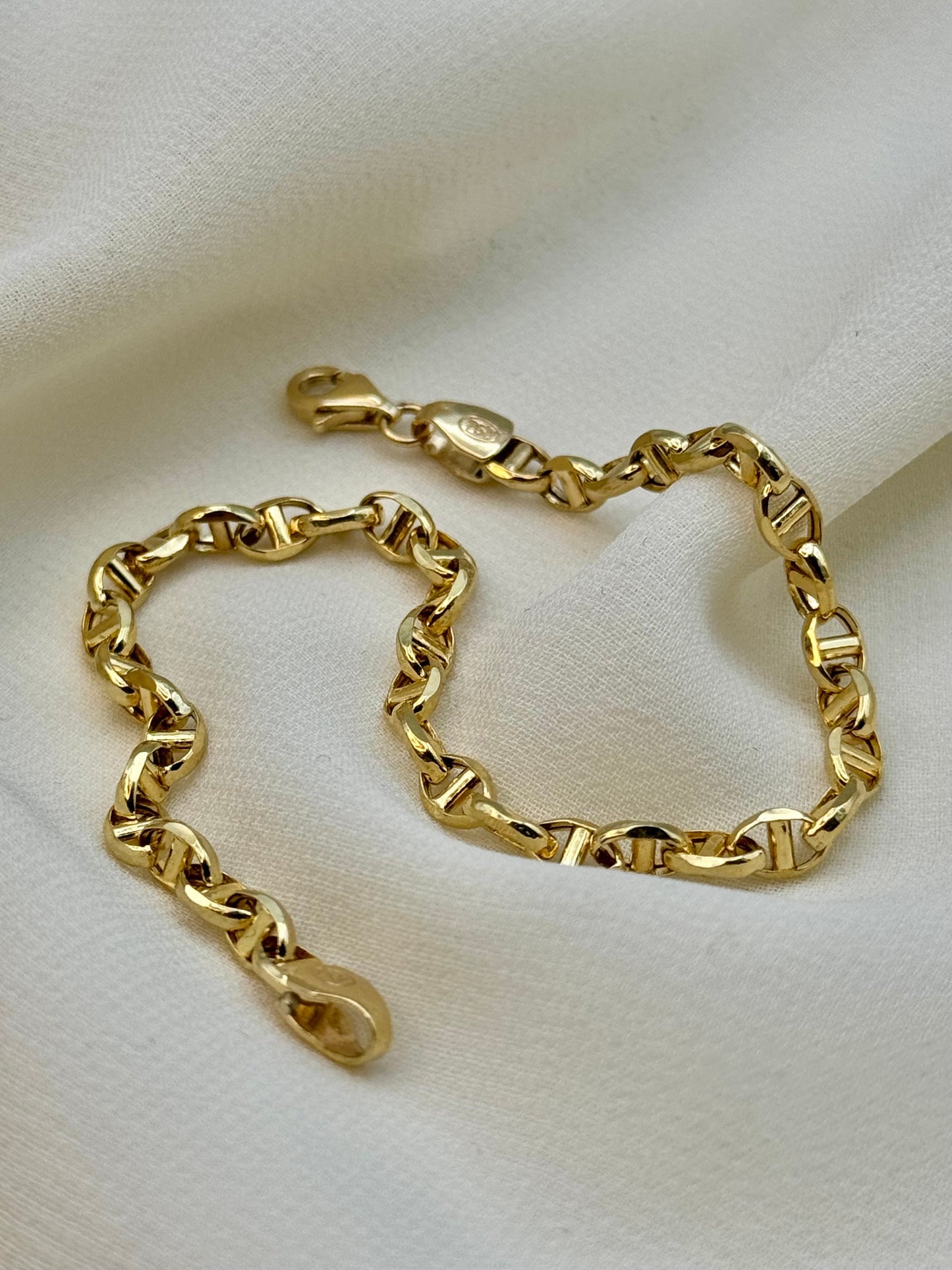 A gold anchor chain bracelet displayed on a white surface.