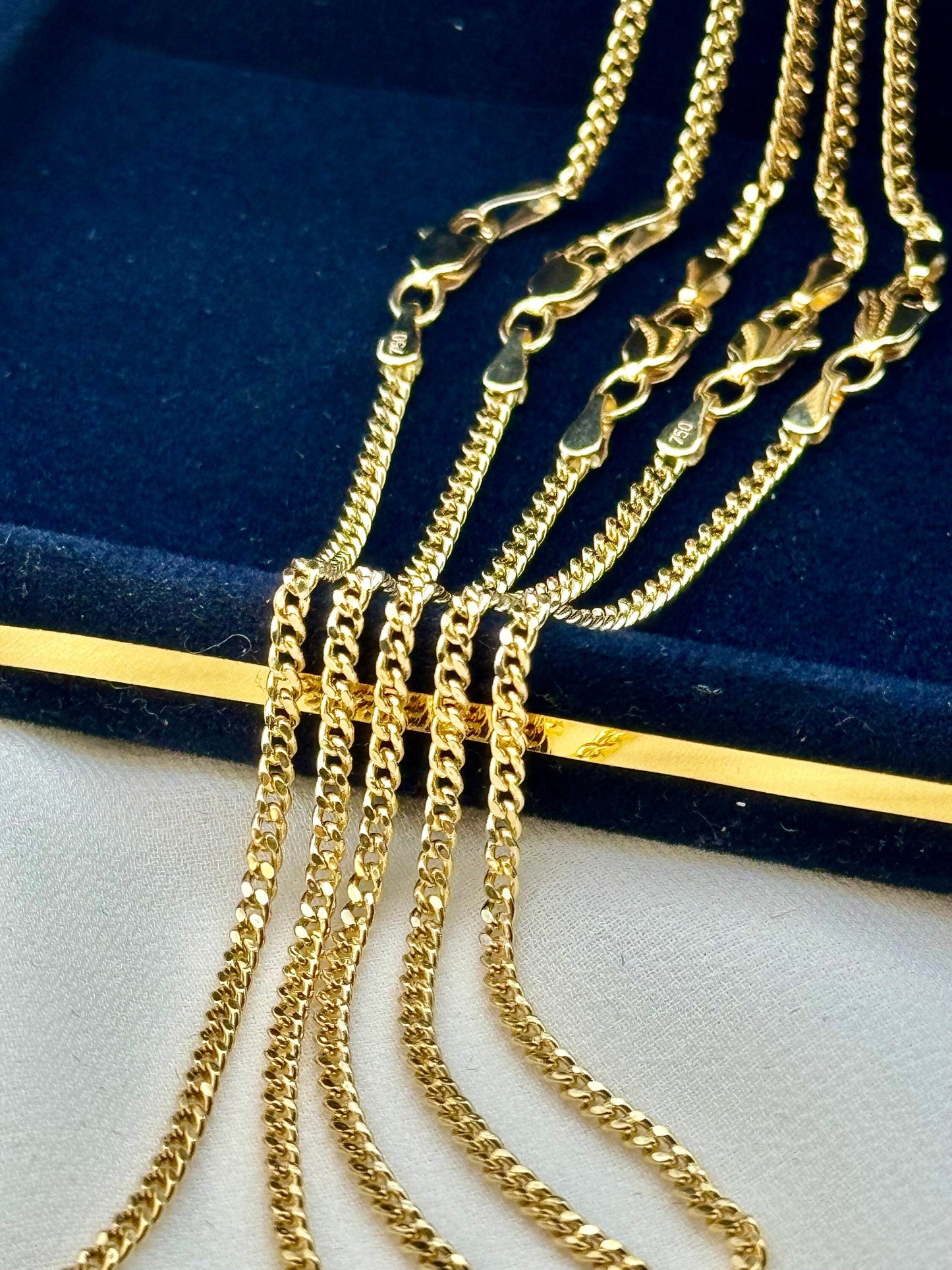 18k gold curb link chain necklace and bracelet on a dark blue background, 2mm width chains.