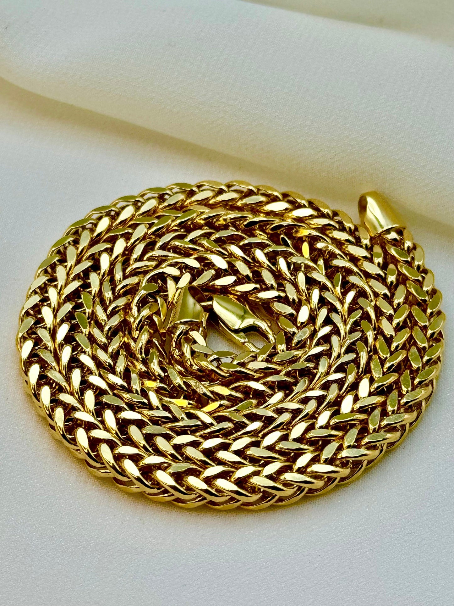 A 14k gold Franco chain necklace with a lobster clasp, displayed on a white fabric surface.