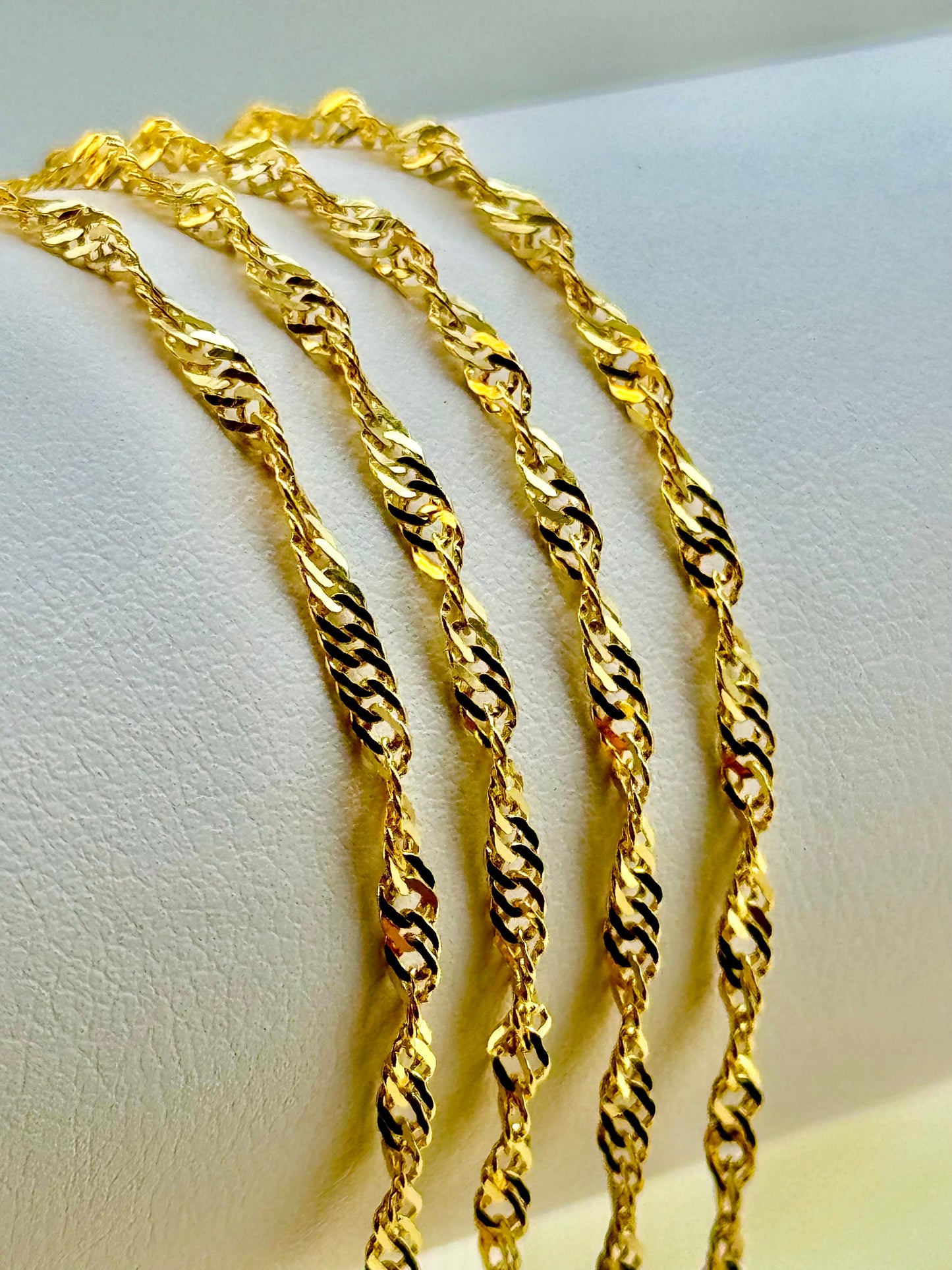 A series of twisted gold chains displayed on a stand, showcasing their shiny and detailed diamond-cut surfaces.