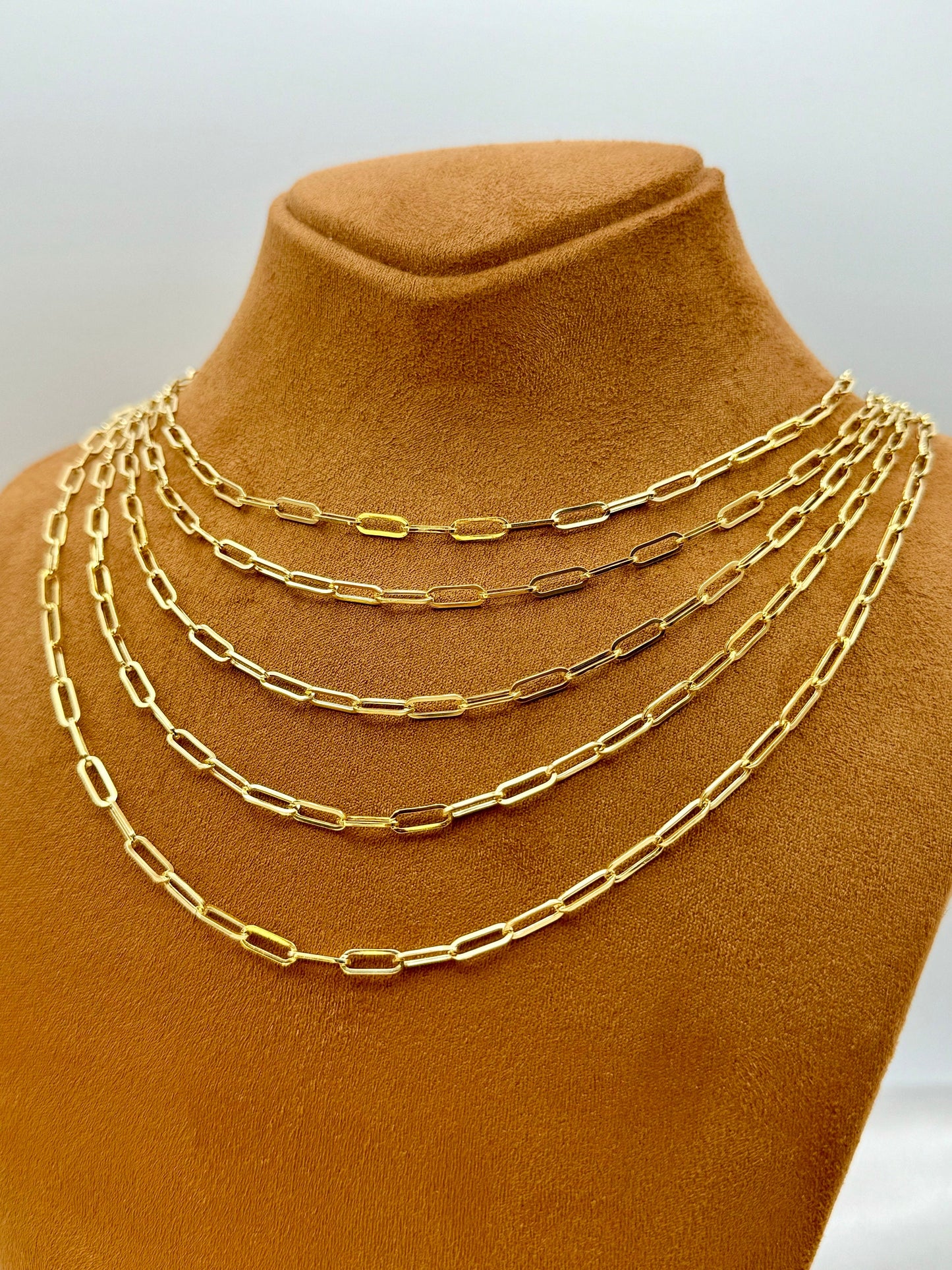 A display of multiple 18K gold paperclip chain necklaces with an oval link design on a mannequin bust.