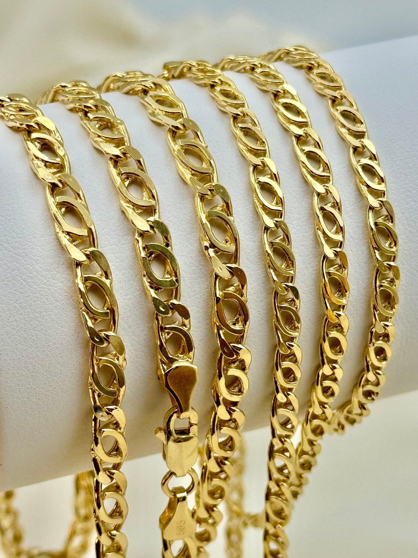 A collection of 14K gold tiger eye cable necklaces with different chain thicknesses displayed on a stand.