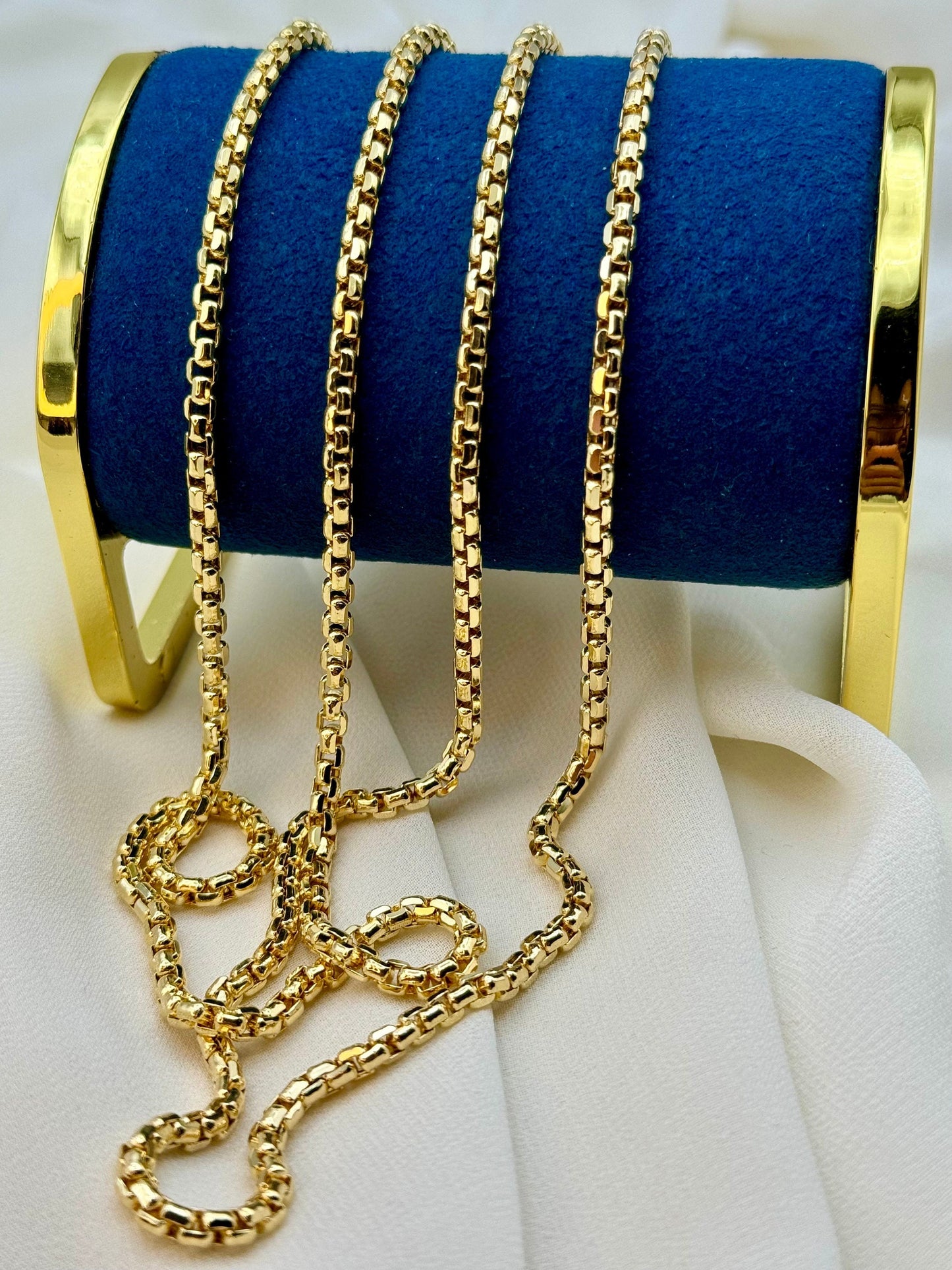 A 14K gold box chain necklace displayed on a blue velvet surface, with a gold-colored clasp.