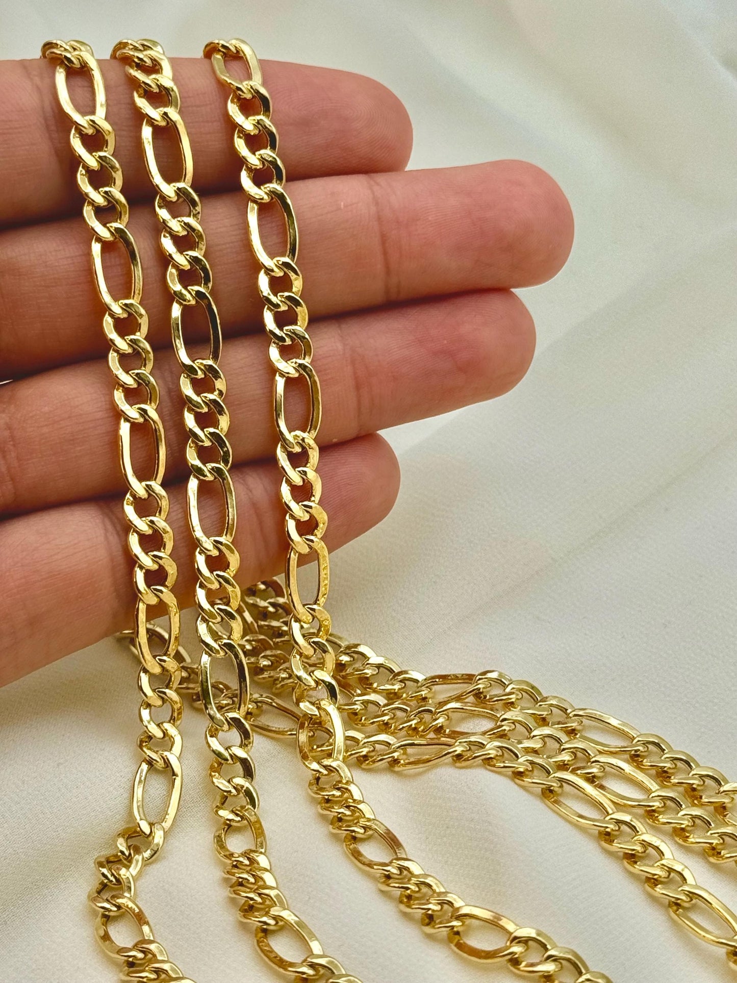 A hand holding a 14k gold figaro chain necklace with a sleek design and a luxurious appearance.