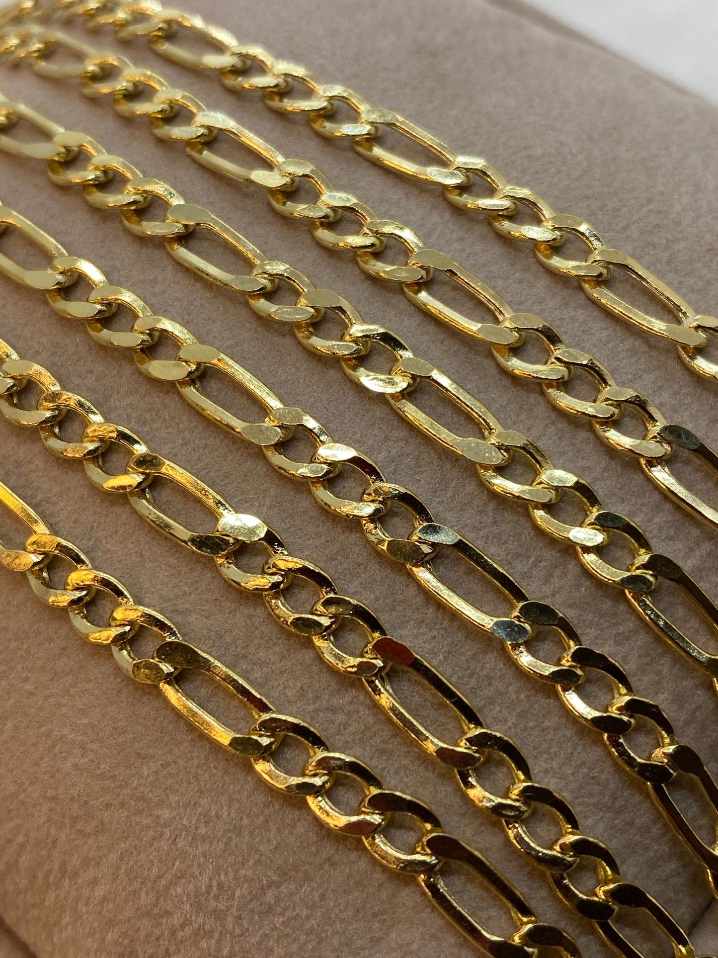 A 14K gold figaro chain necklace laid out on a textured surface.