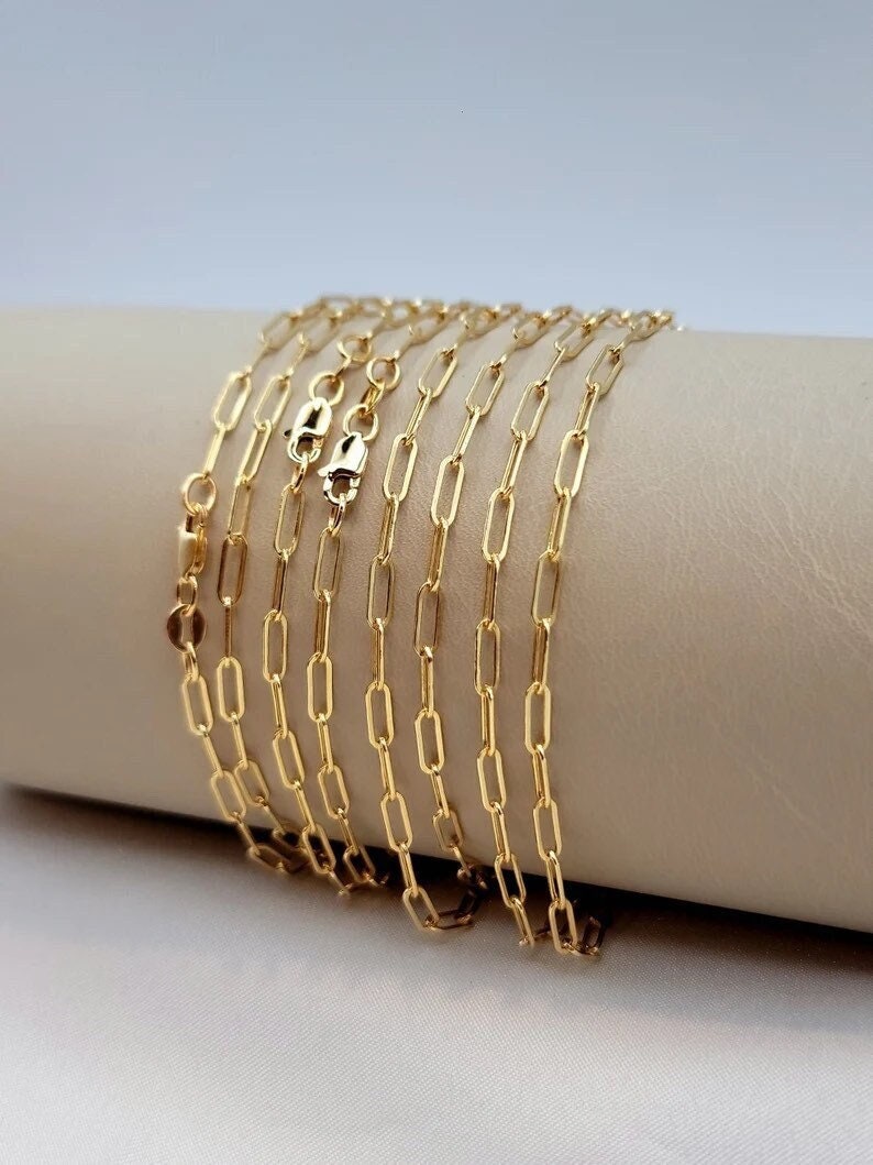 An 18K gold paperclip chain necklace displayed on a mannequin bust, showcasing the oval link design and the lobster claw closure.