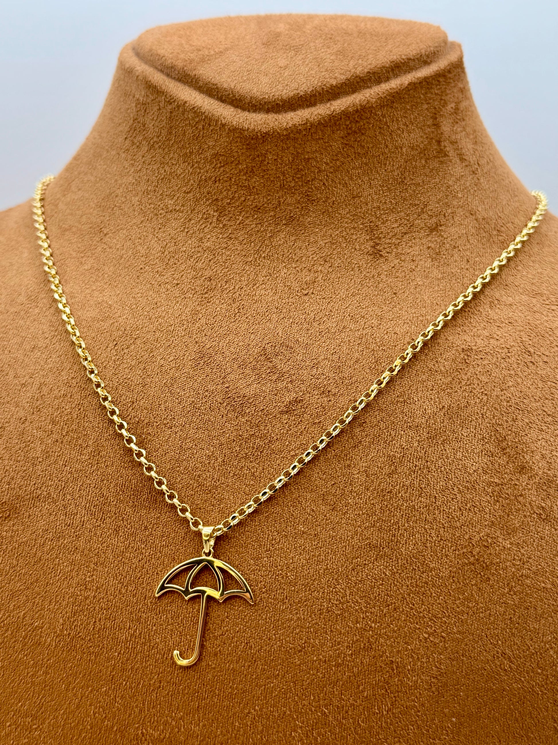 Gold necklace with an umbrella pendant on a brown velvet mannequin.