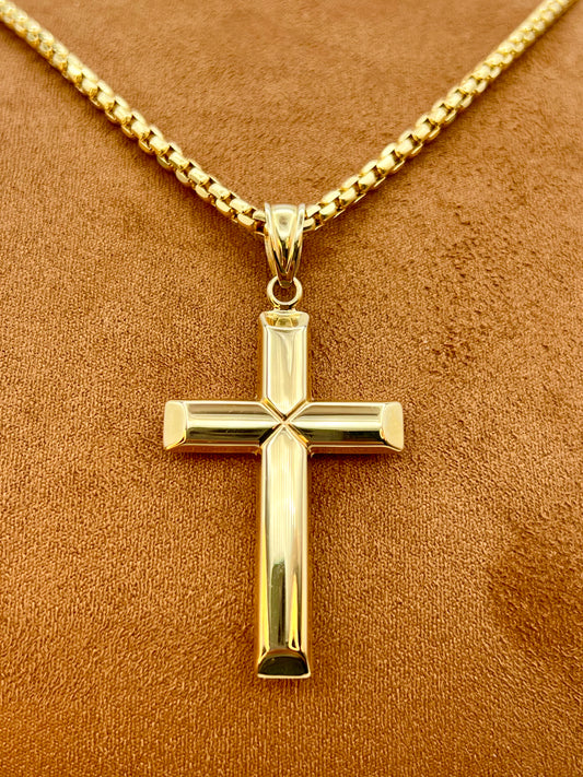 A polished yellow gold cross pendant necklace on a matching gold chain, displayed on a textured brown surface.