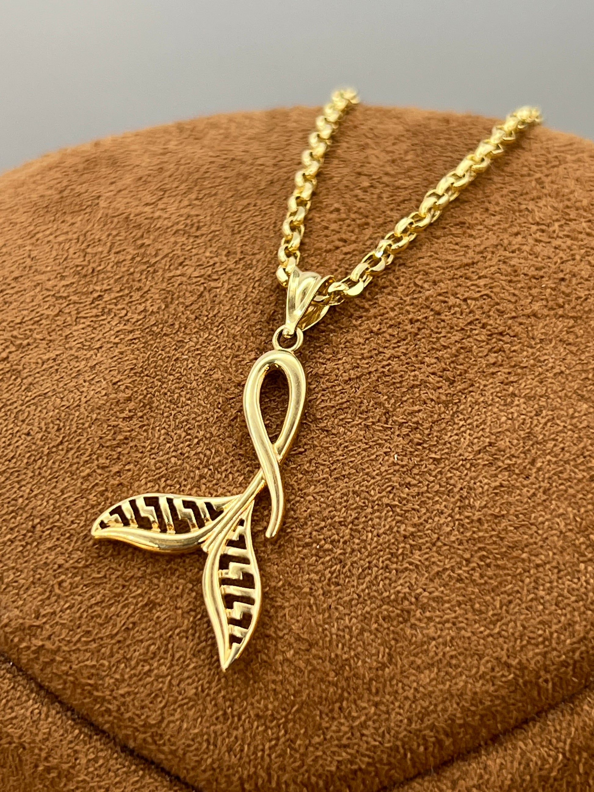 A gold necklace with a pendant combining an whale tail symbol, displayed on a brown textured jewelry bust.