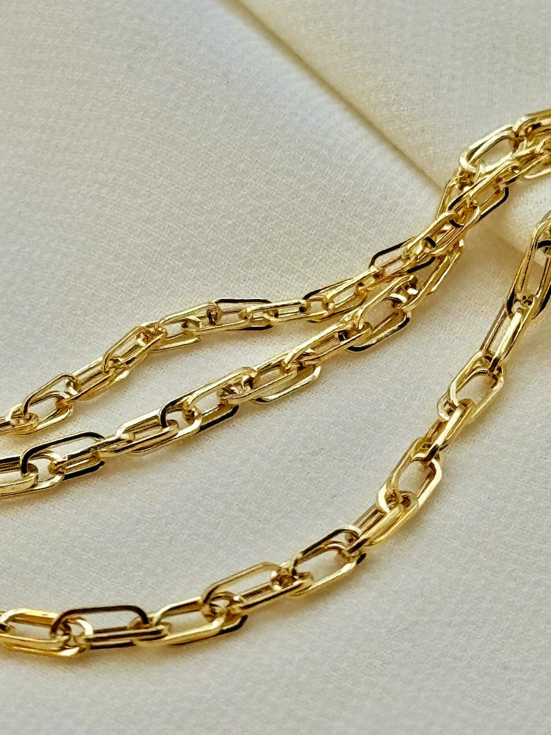 A close-up of a gold paperclip chain draped diagonally across a textured cream-colored surface.