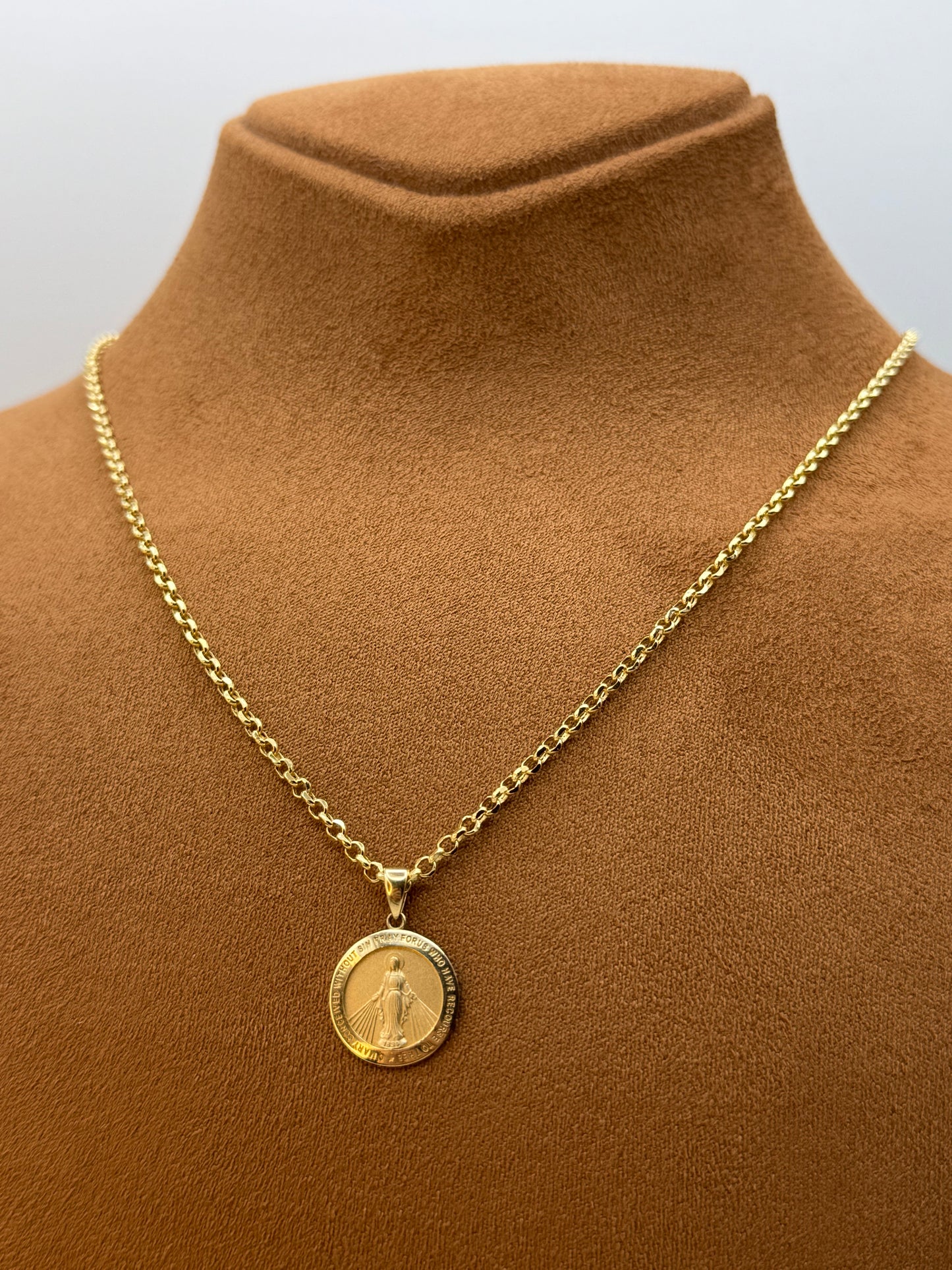 Gold chain necklace with a round virgin merry pendant on a brown garment.