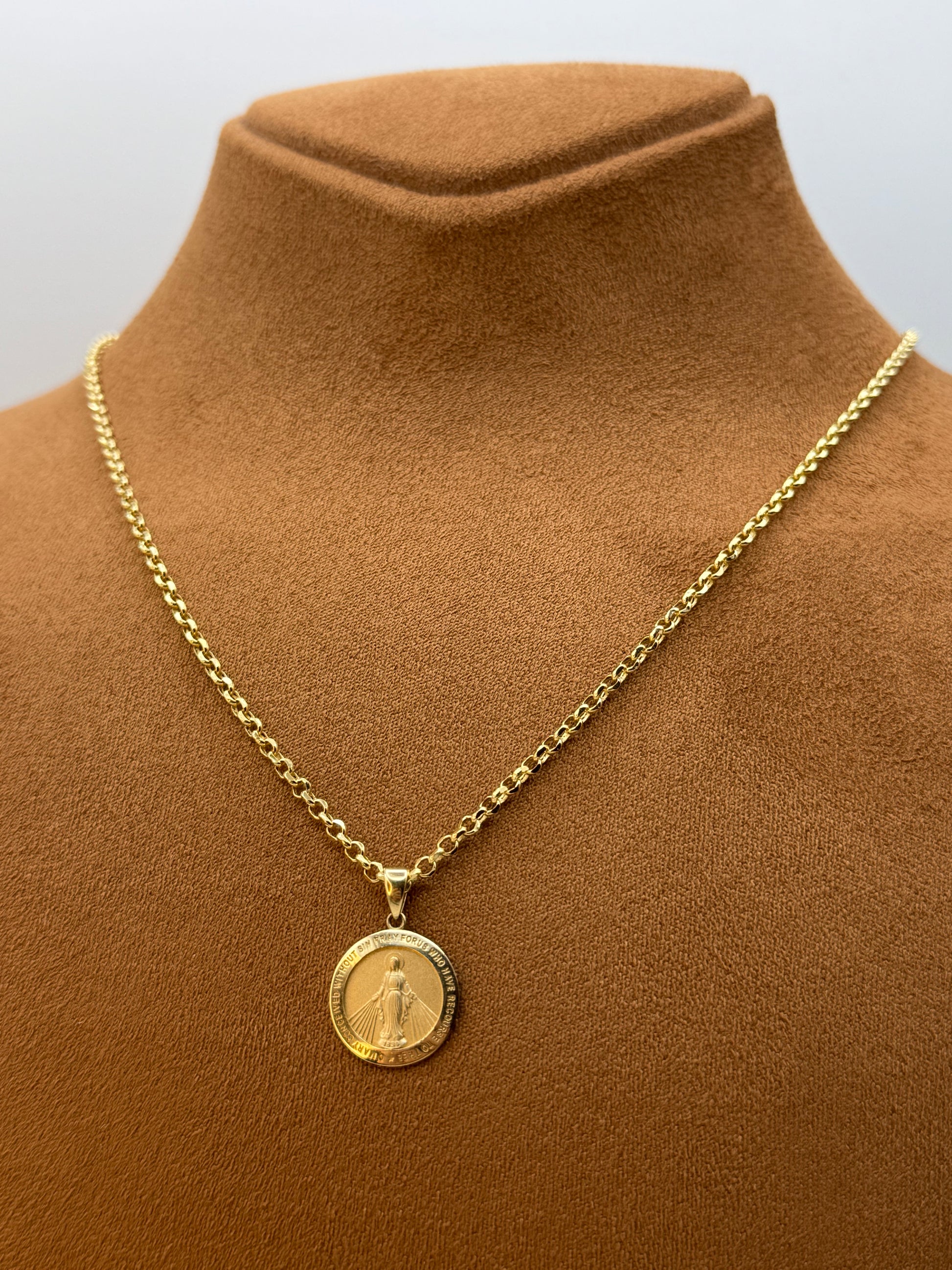Gold chain necklace with a round virgin merry pendant on a brown garment.