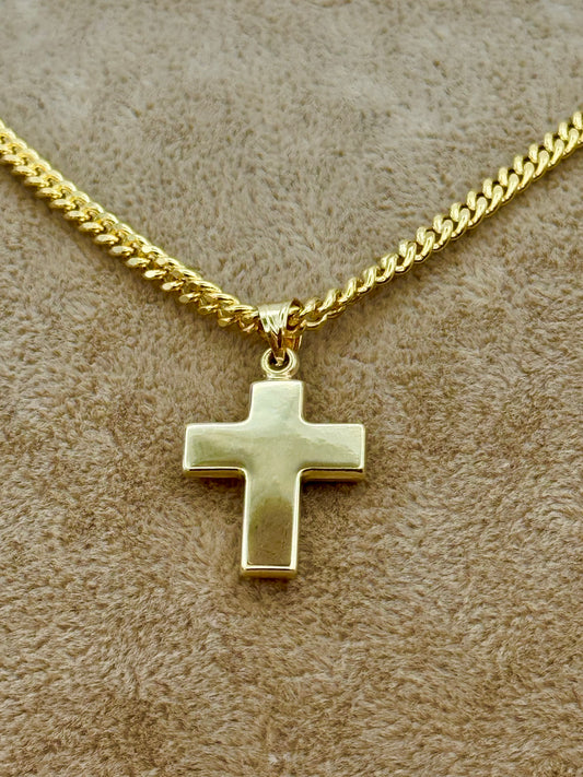 A gold cross pendant necklace on a gold chain, displayed on a textured beige fabric background.