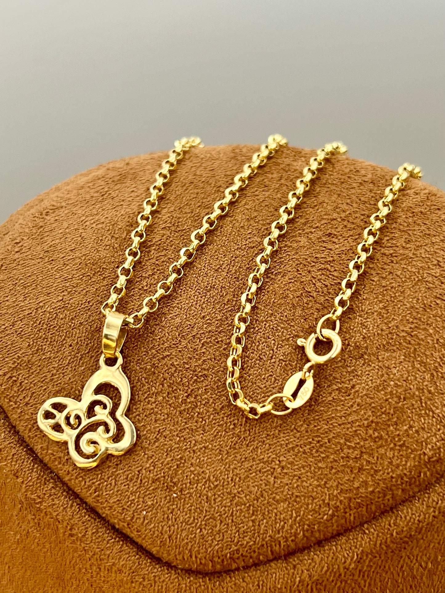 A gold-tone chain necklace with a butterfly pendant, displayed on a brown textured jewelry stand against a neutral gray background.