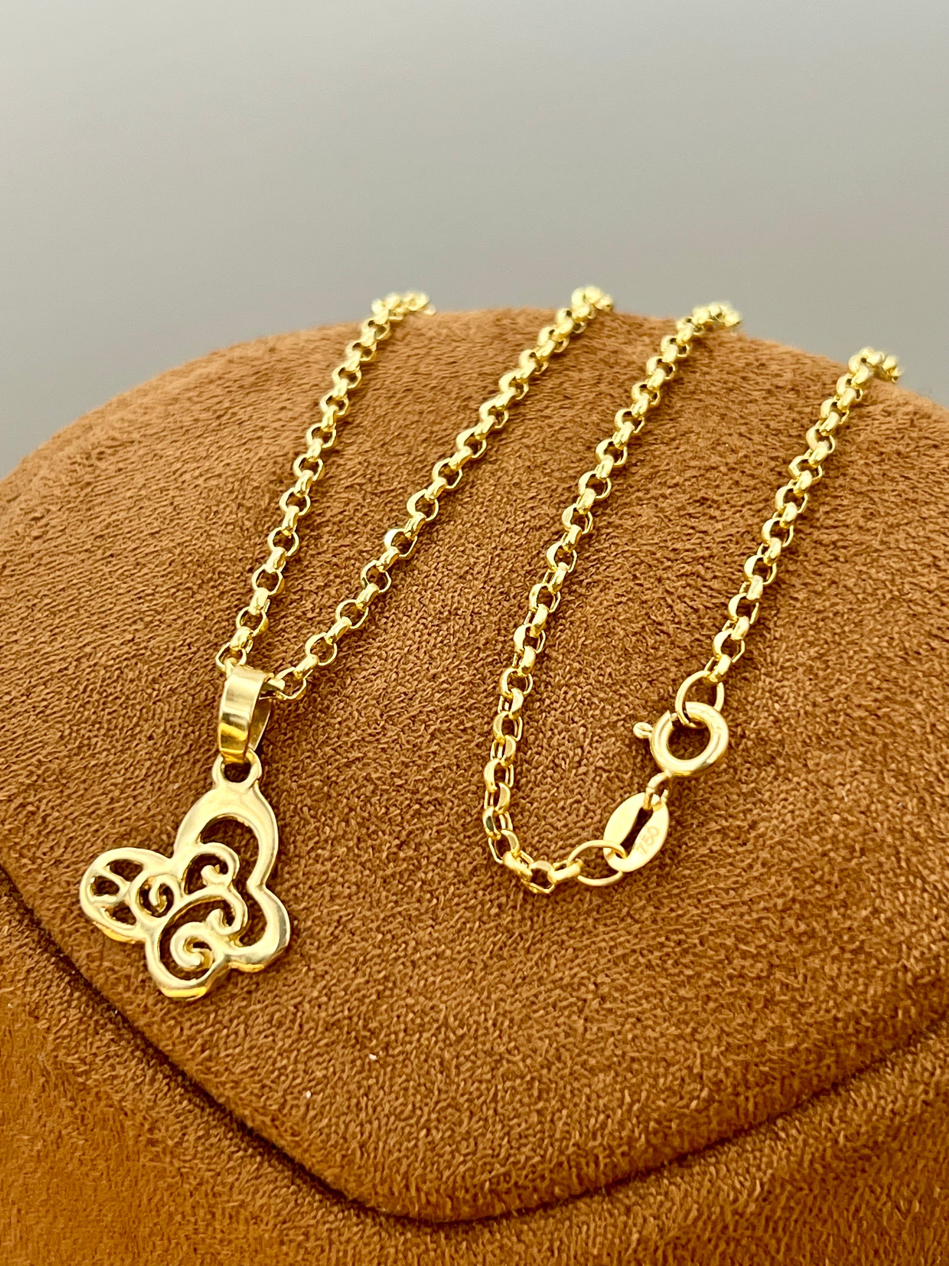 A gold-tone chain necklace with a butterfly pendant, displayed on a brown textured jewelry stand against a neutral gray background.