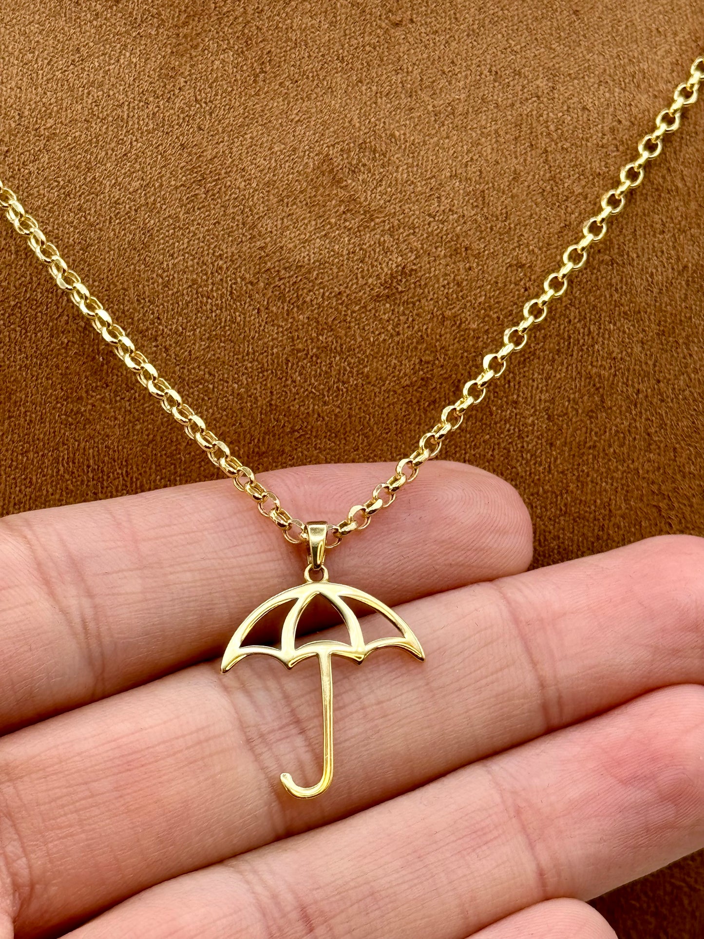 Gold umbrella necklace on a hand with a brown background