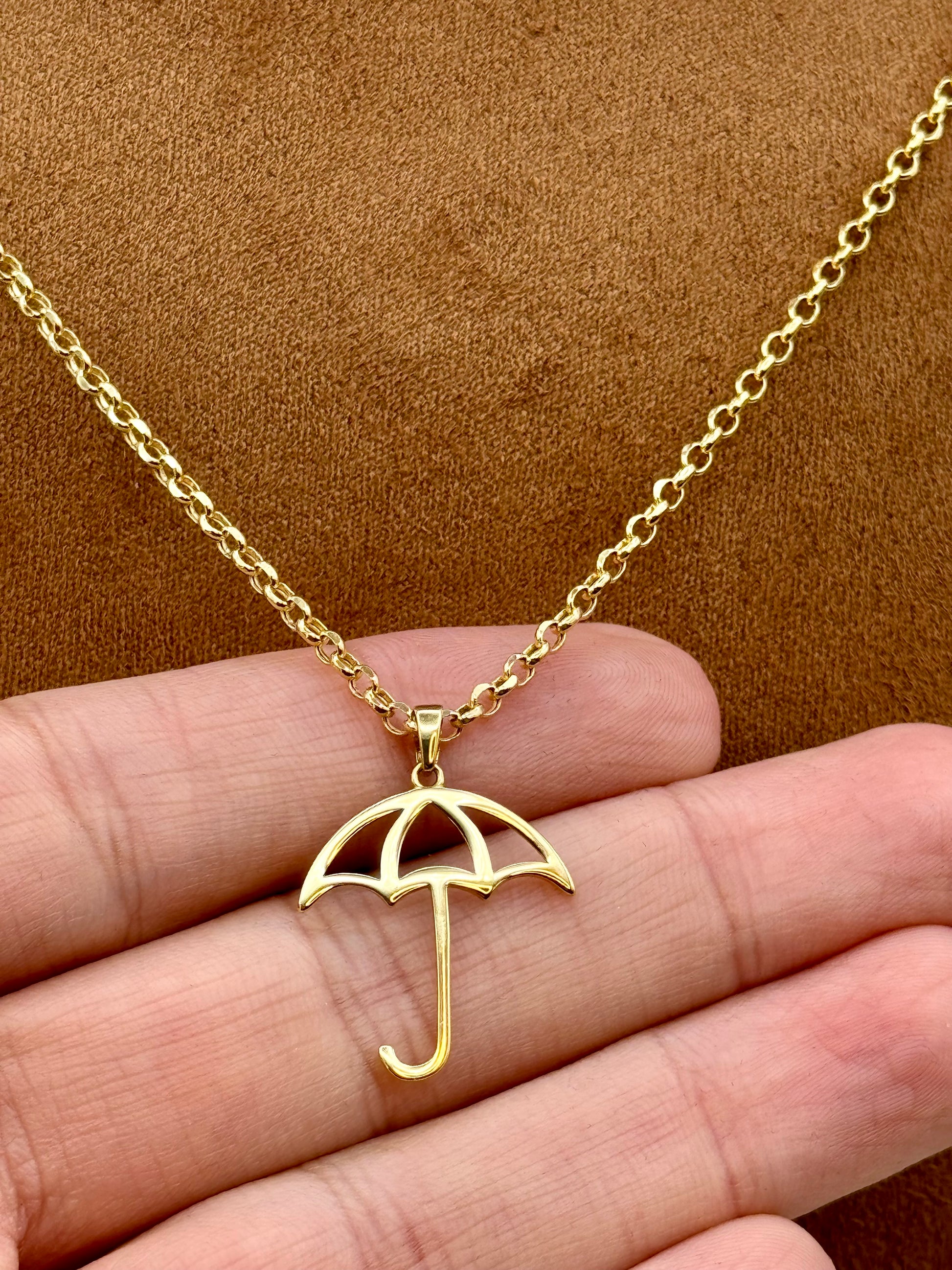 Gold umbrella necklace on a hand with a brown background