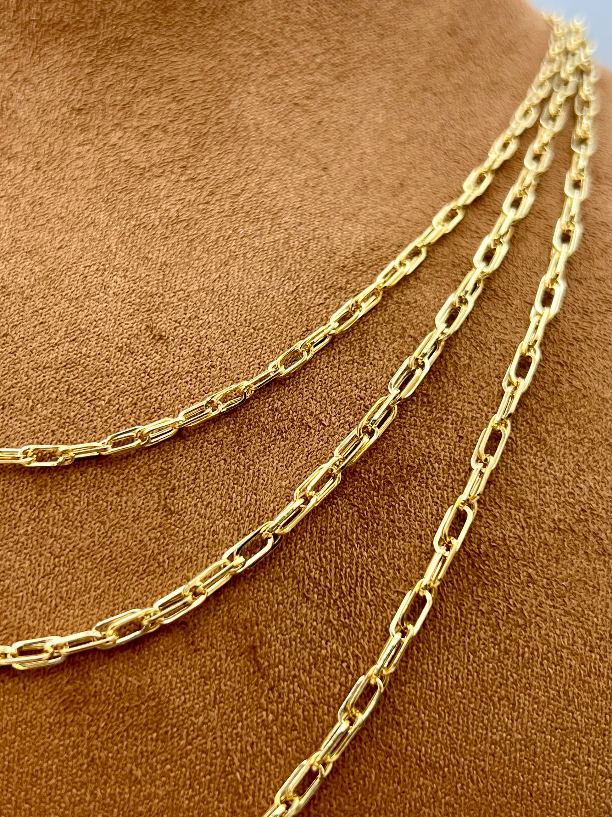 A close-up of a gold paperclip chain necklace draped over a brown suede or velvet jewelry display bust.