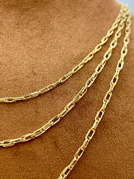 A close-up of a gold paperclip chain necklace draped over a brown suede or velvet jewelry display bust.