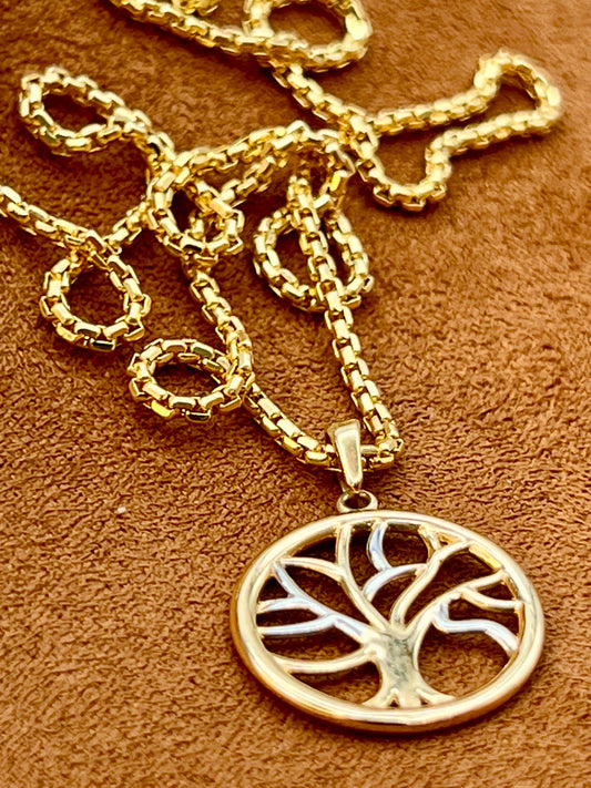 A 14k gold-tone necklace with a circular tree of life pendant, displayed on a textured brown surface.