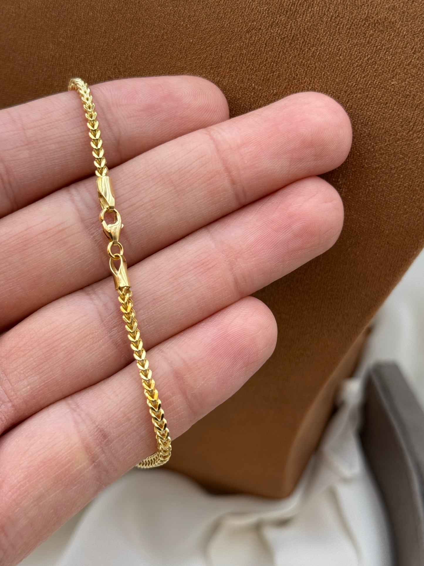 Gold bracelet on a person's wrist with a brown leather surface in the background