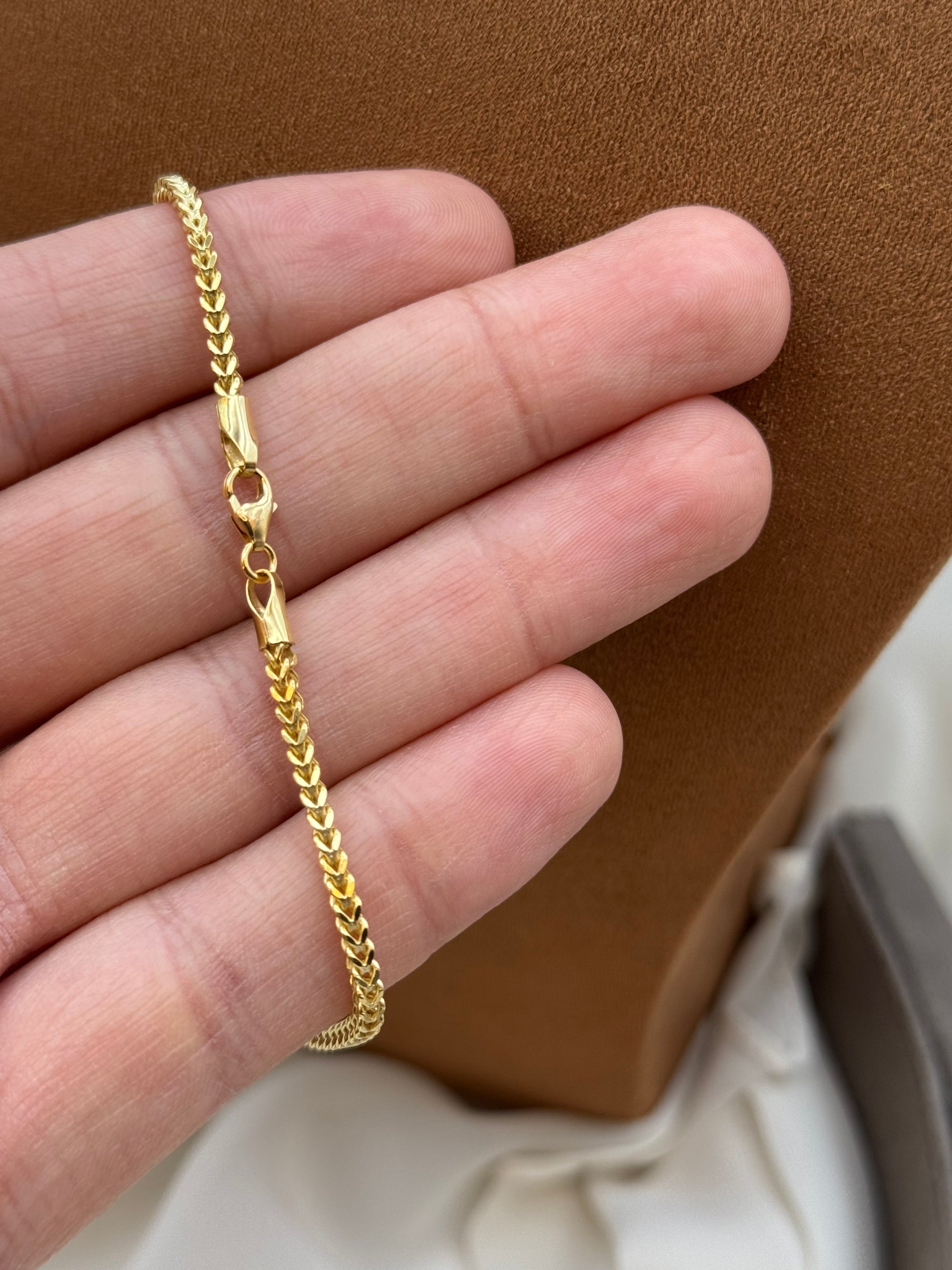 Gold bracelet on a person's wrist with a brown leather surface in the background