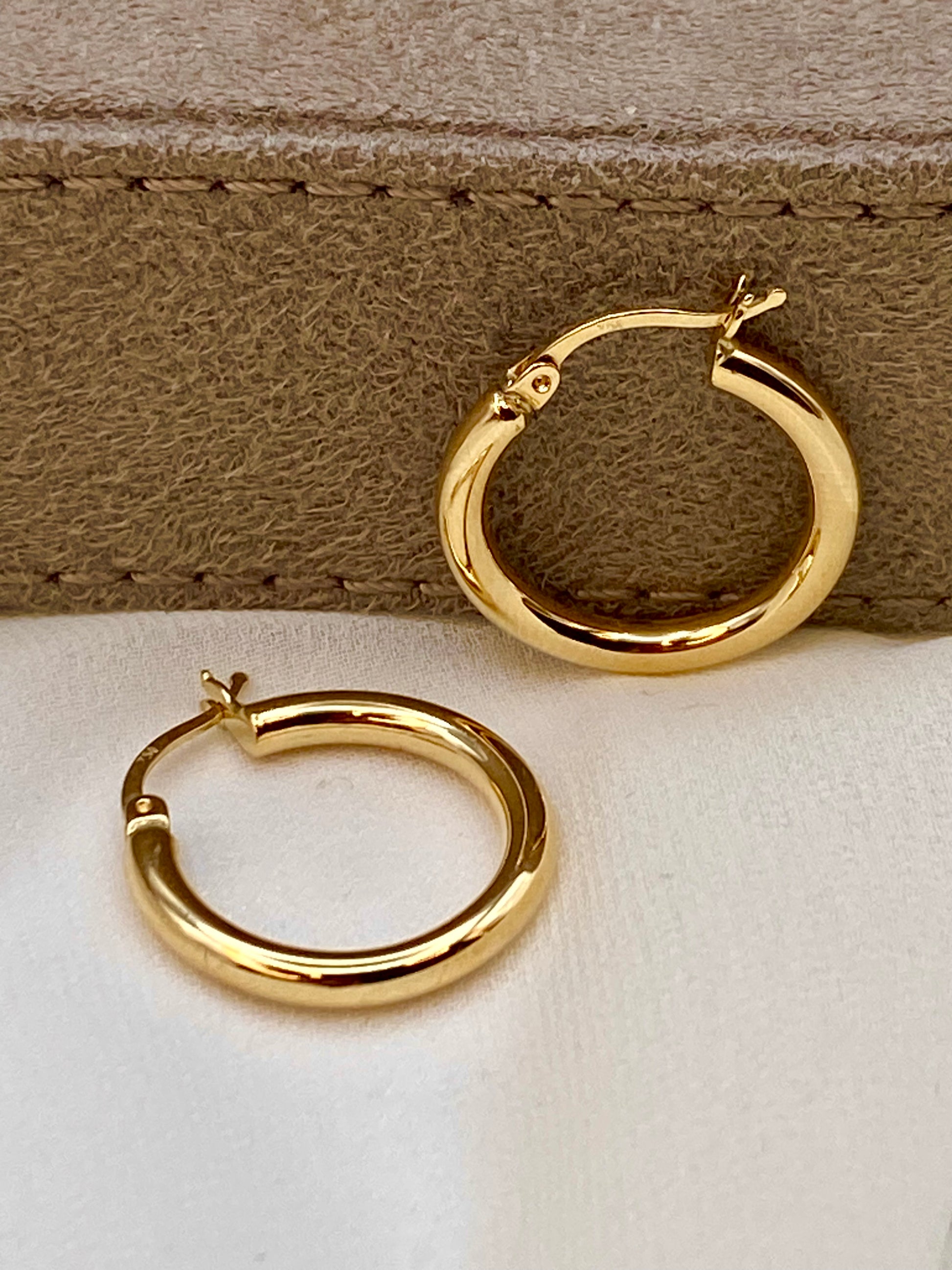 18k Gold hoop earrings on a beige leather surface