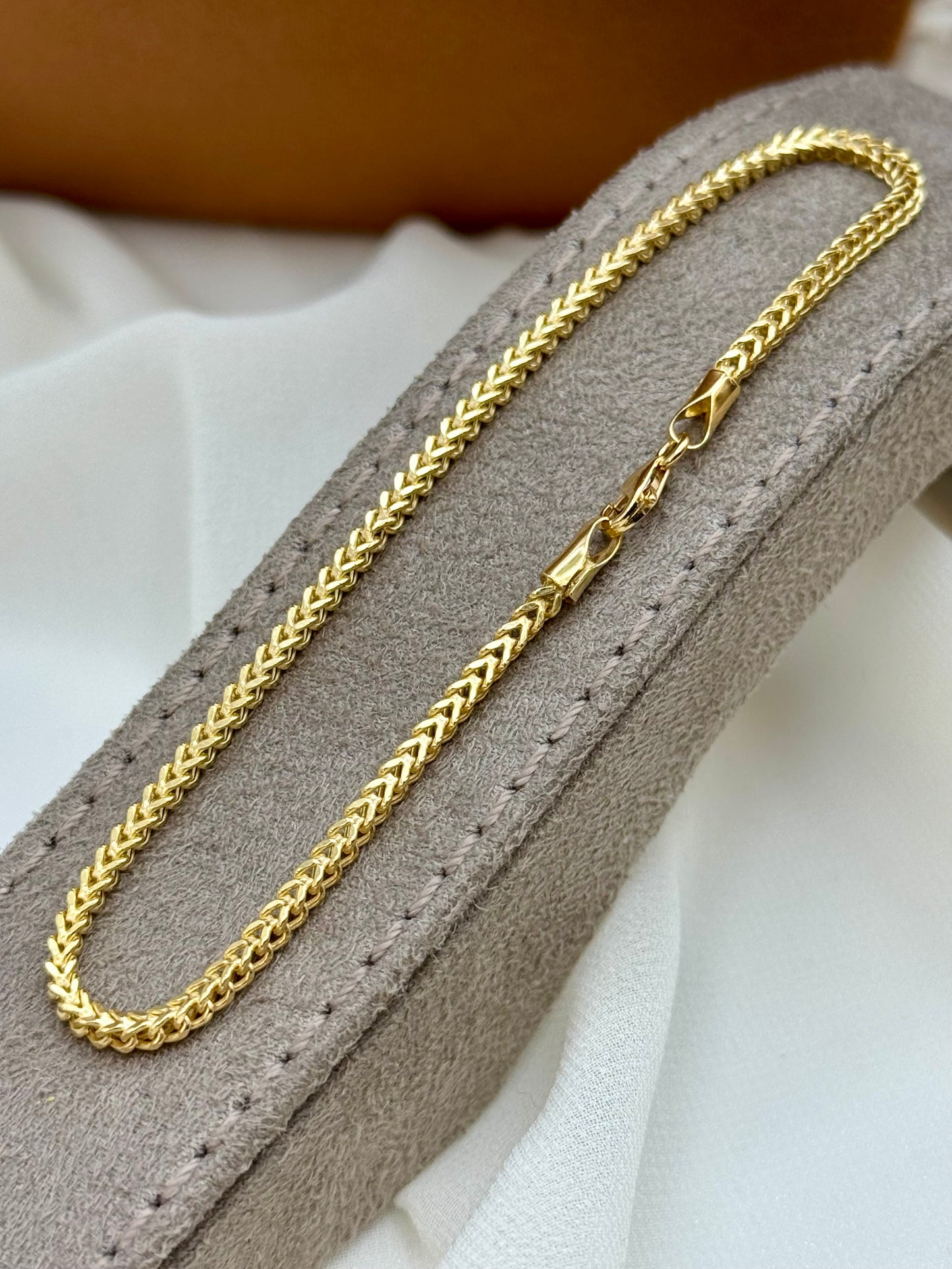 Franco Gold chain Bracelet on a gray cushion with a white background