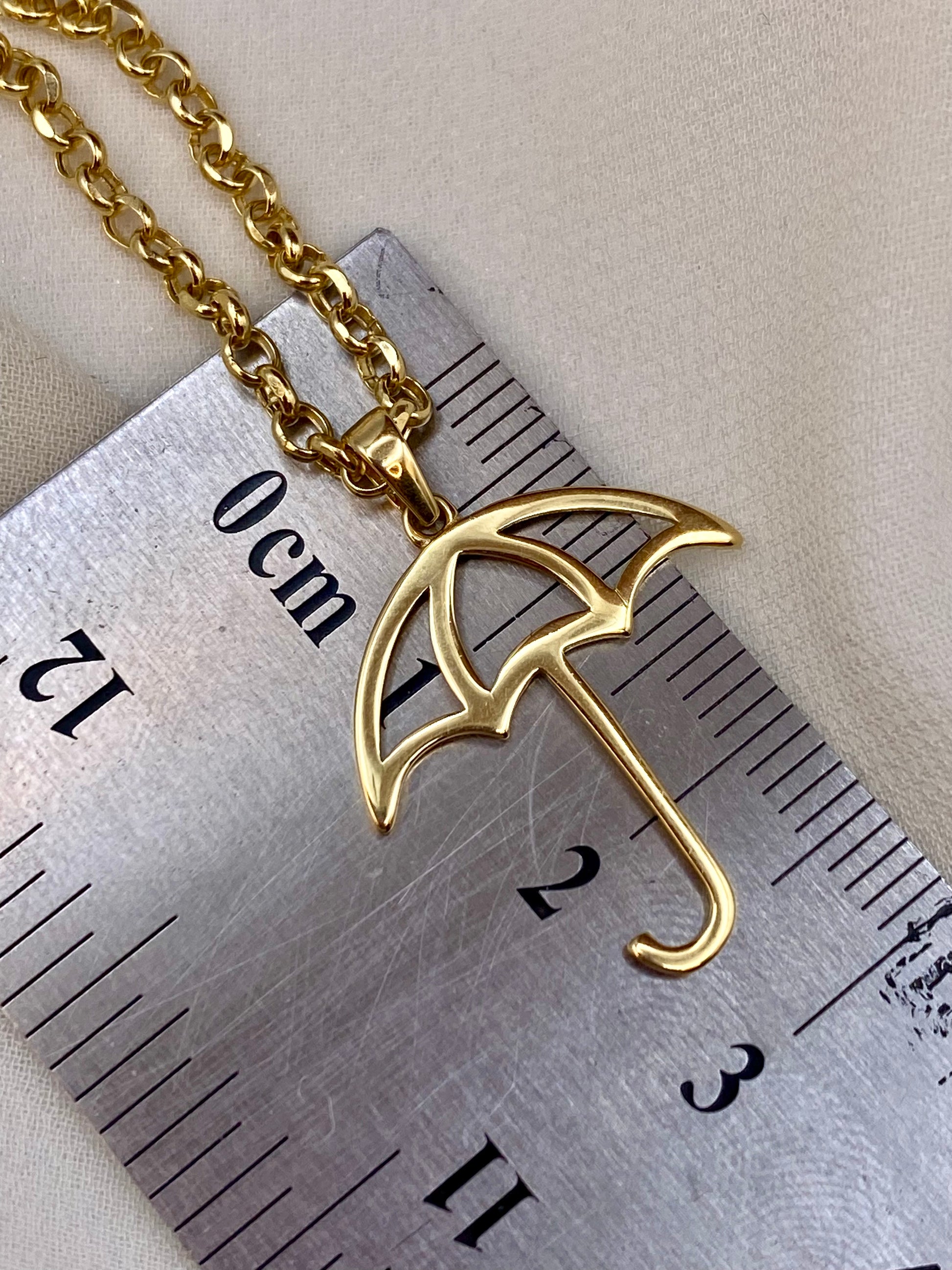 Gold umbrella-shaped pendant on a chain next to a ruler for scale.
