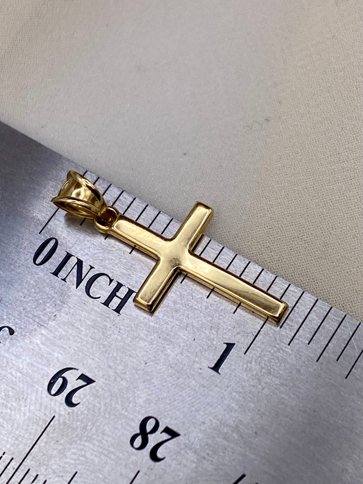 Gold cross pendant on a ruler for scale