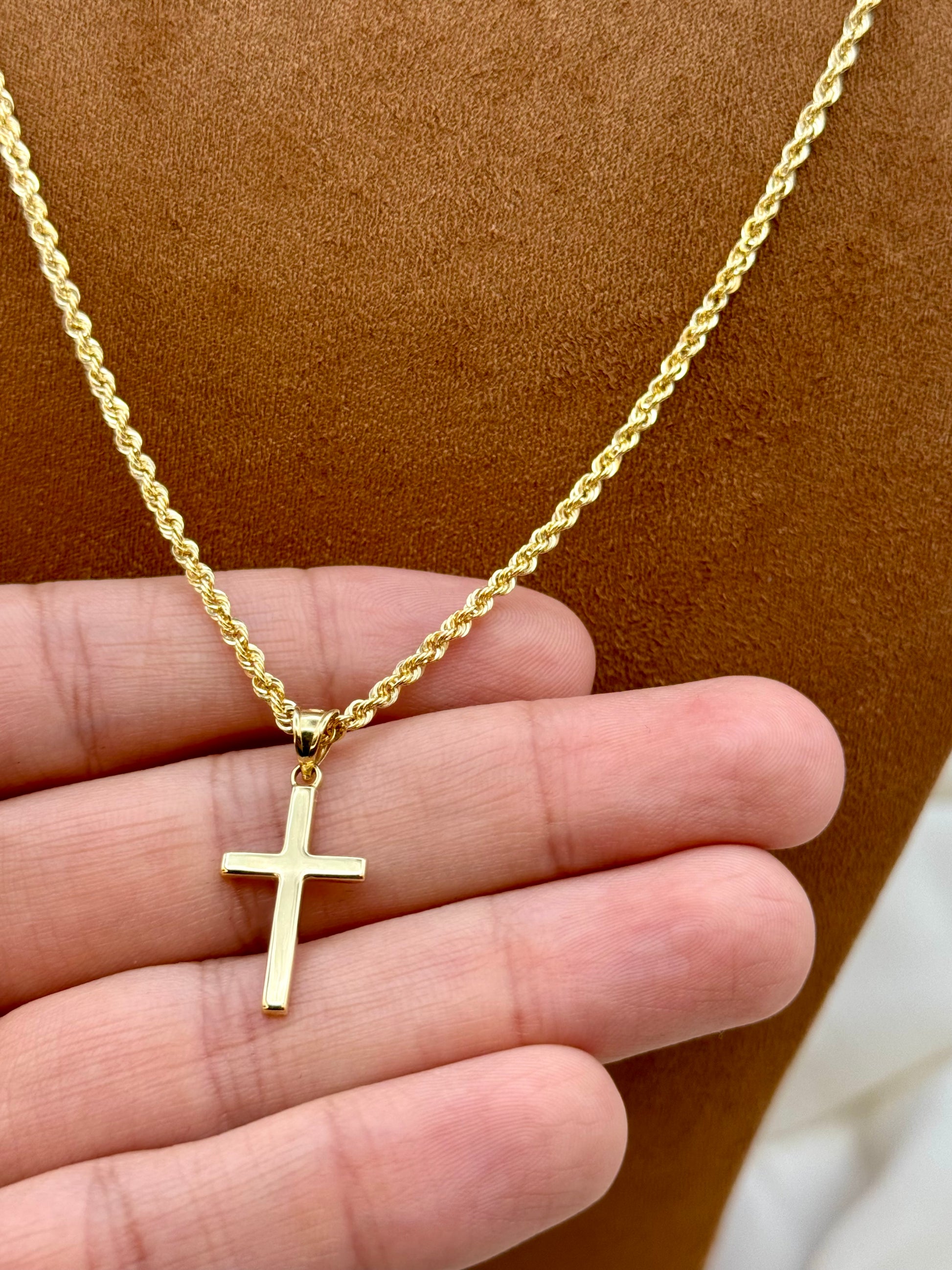18k Gold necklace with a cross pendant held in a hand against a brown background