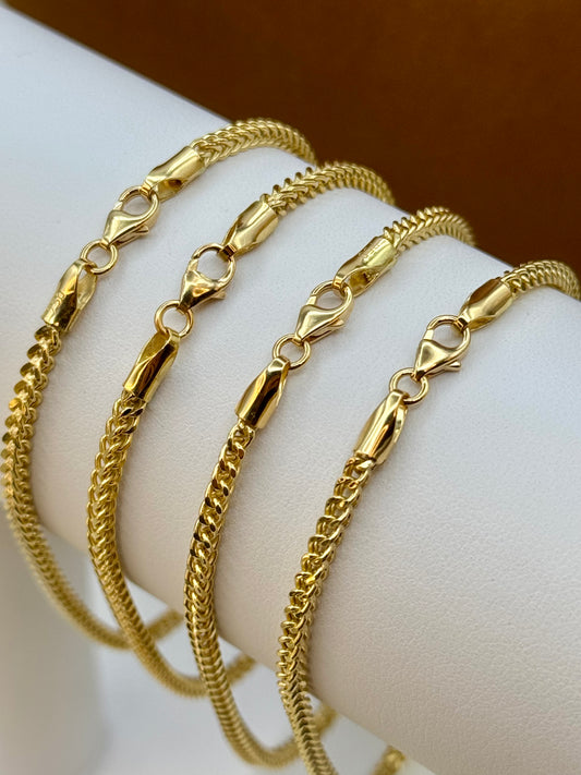 Four 18k gold Franco bracelets on a white wrist against a brown background
