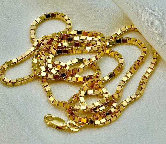 A 18k gold box chain necklace with a lobster clasp, coiled on a white textured fabric background.