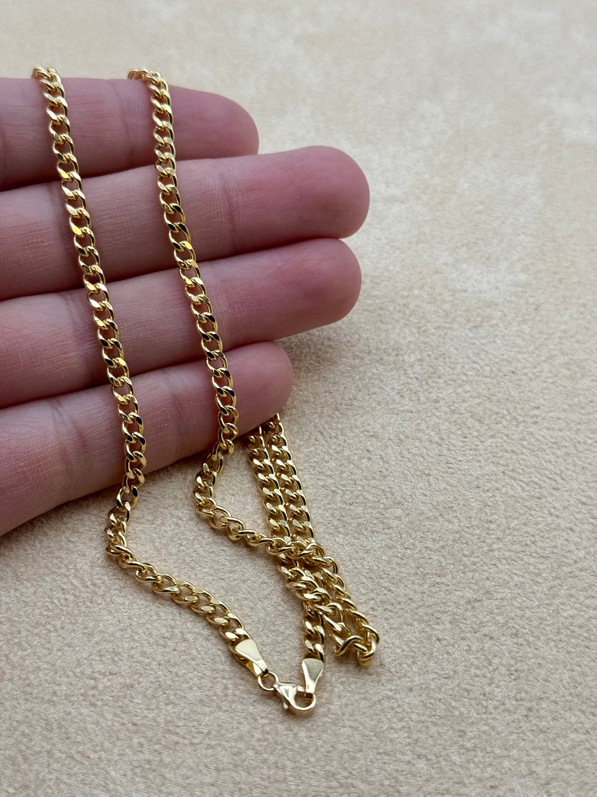 18k Gold curb chain held between fingers on a beige background