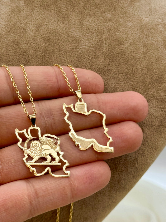 Two 18k gold Iran map necklaces held in a hand against a brown background