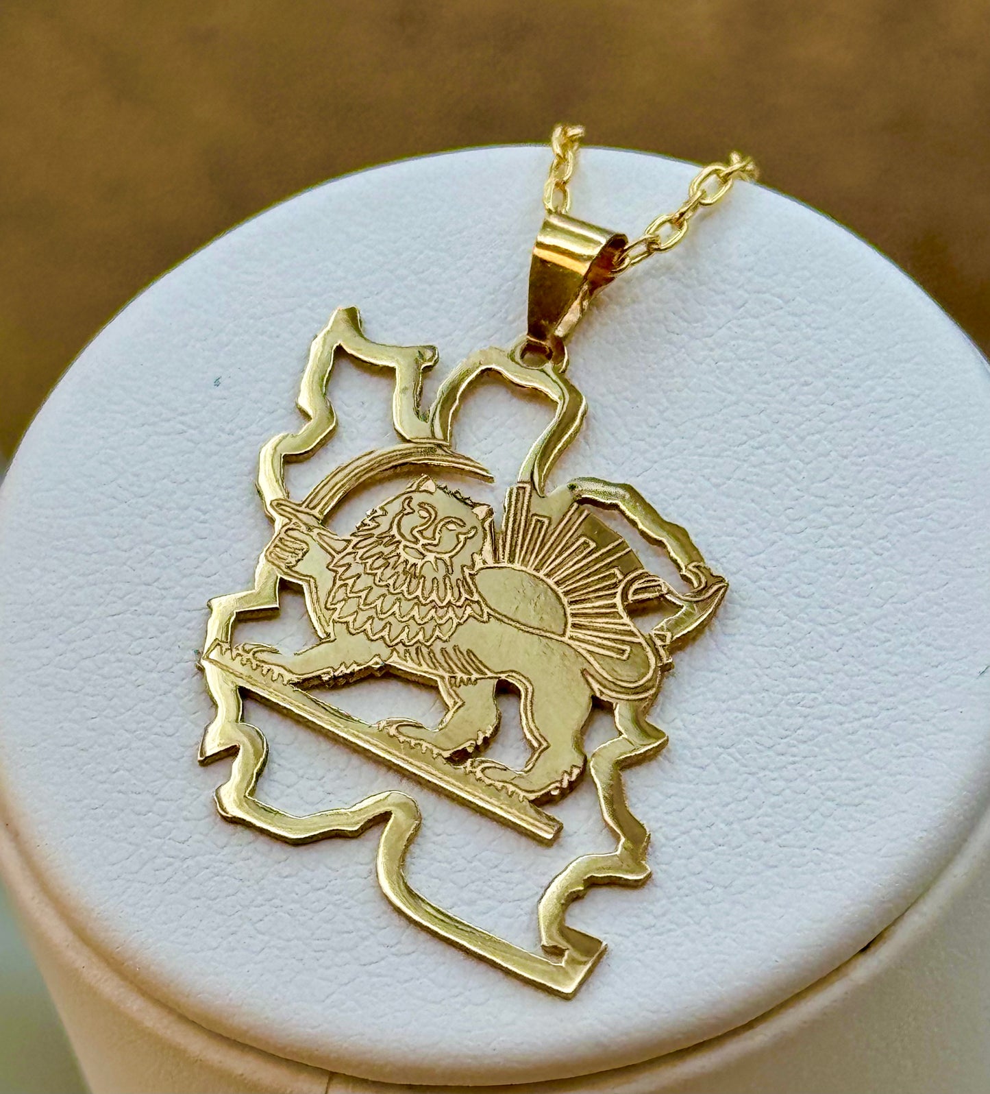 18k Gold lion and sun pendant on a white stand with a brown background